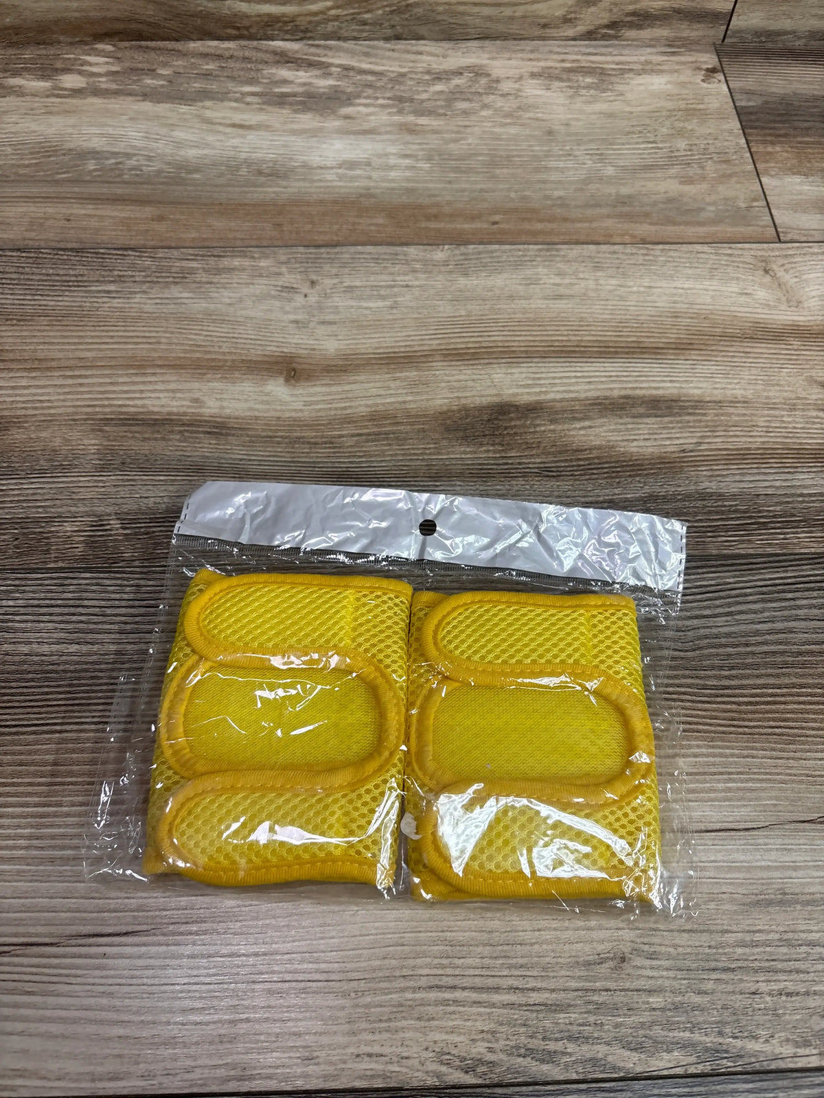 A pair of yellow Lipfer baby crawling knee pads in a clear plastic package on a wooden surface.