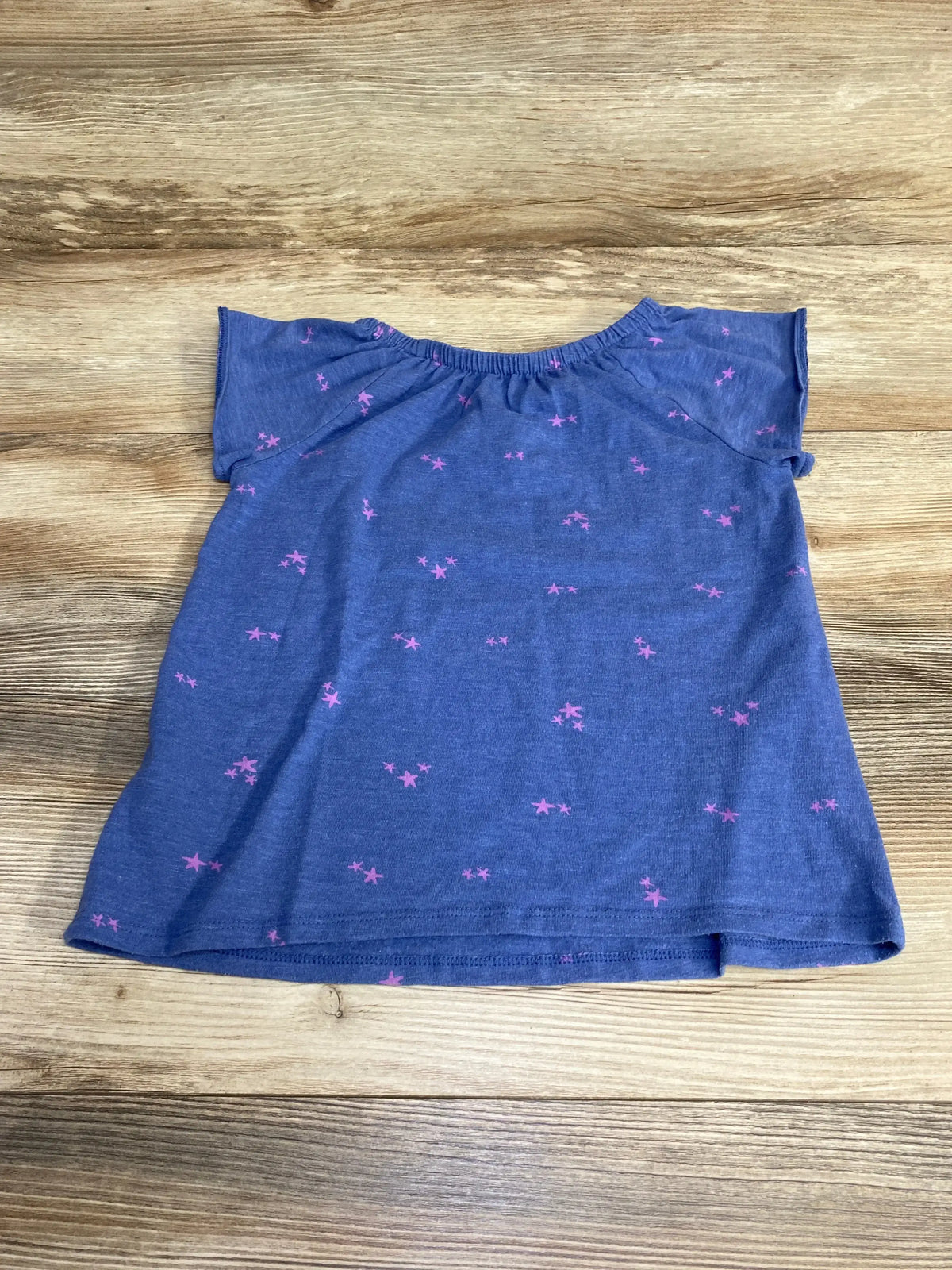 Flat lay of Cat & Jack blue toddler shirt showing pink star print and ruffled cap sleeves on wood background
