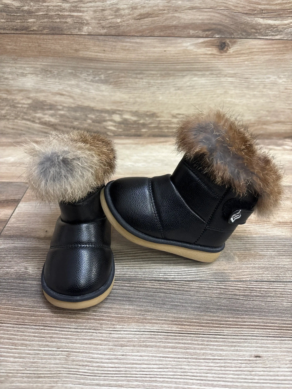 Black toddler boots with faux fur trim and rubber soles on a wood background