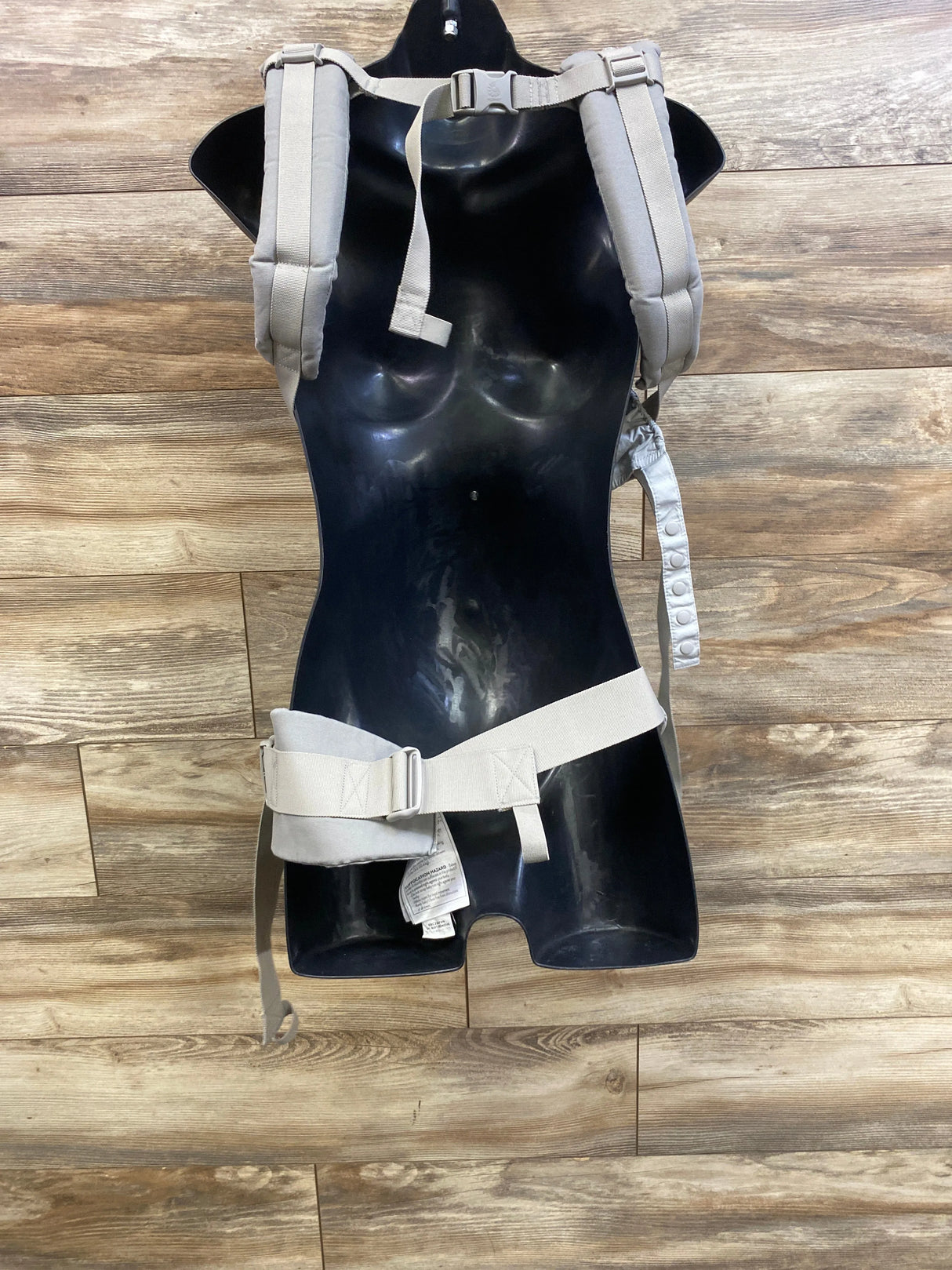 Front view of Ergobaby Omni 360 carrier in Pearl Grey showing padded shoulder straps and wide waist belt on wood floor