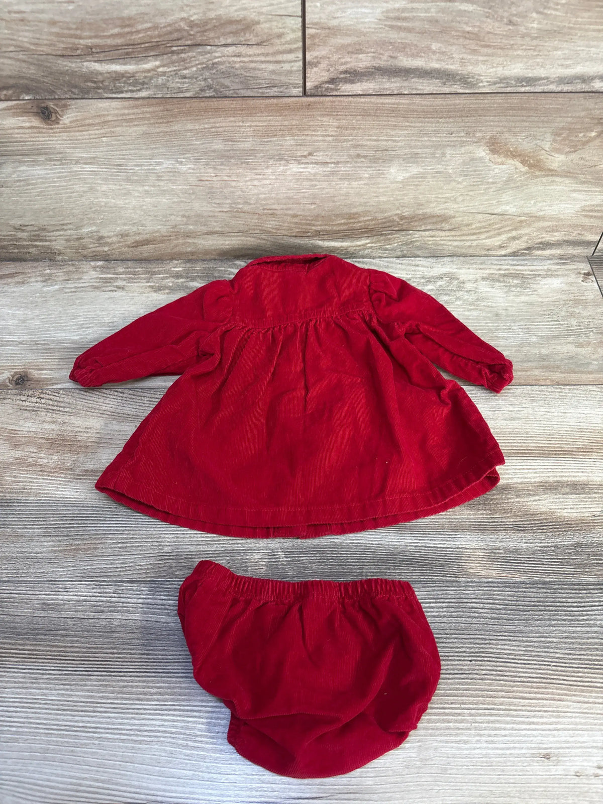 Front view of Carter’s newborn red corduroy dress and bloomers set showcasing the button-front dress on wood-grain background