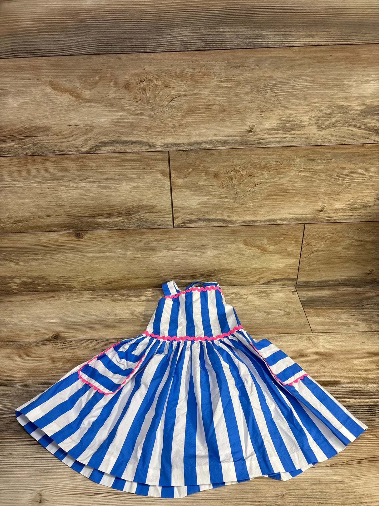 Flat lay of Jacadi toddler blue and white striped sleeveless dress showing pink ricrac trim and gathered skirt on wood floor