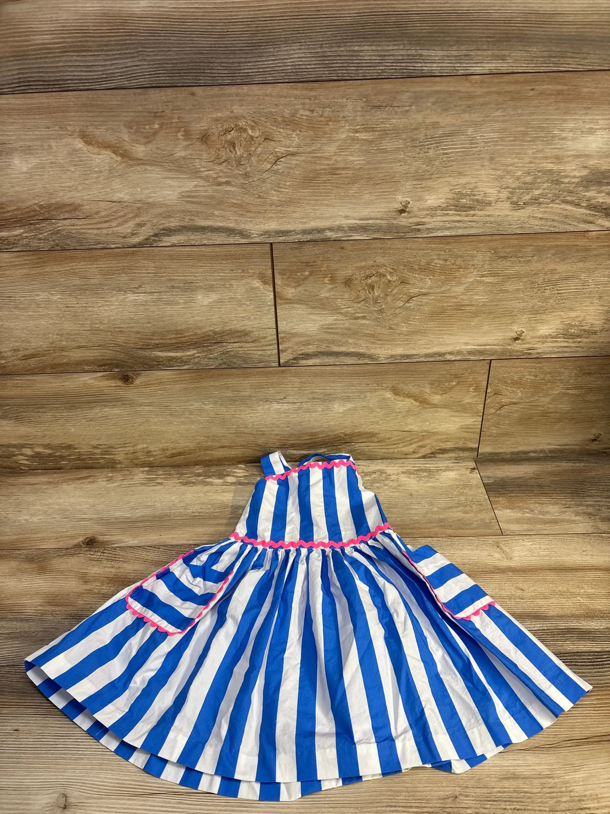 Flat lay of Jacadi toddler blue and white striped sleeveless dress showing pink ricrac trim and gathered skirt on wood floor