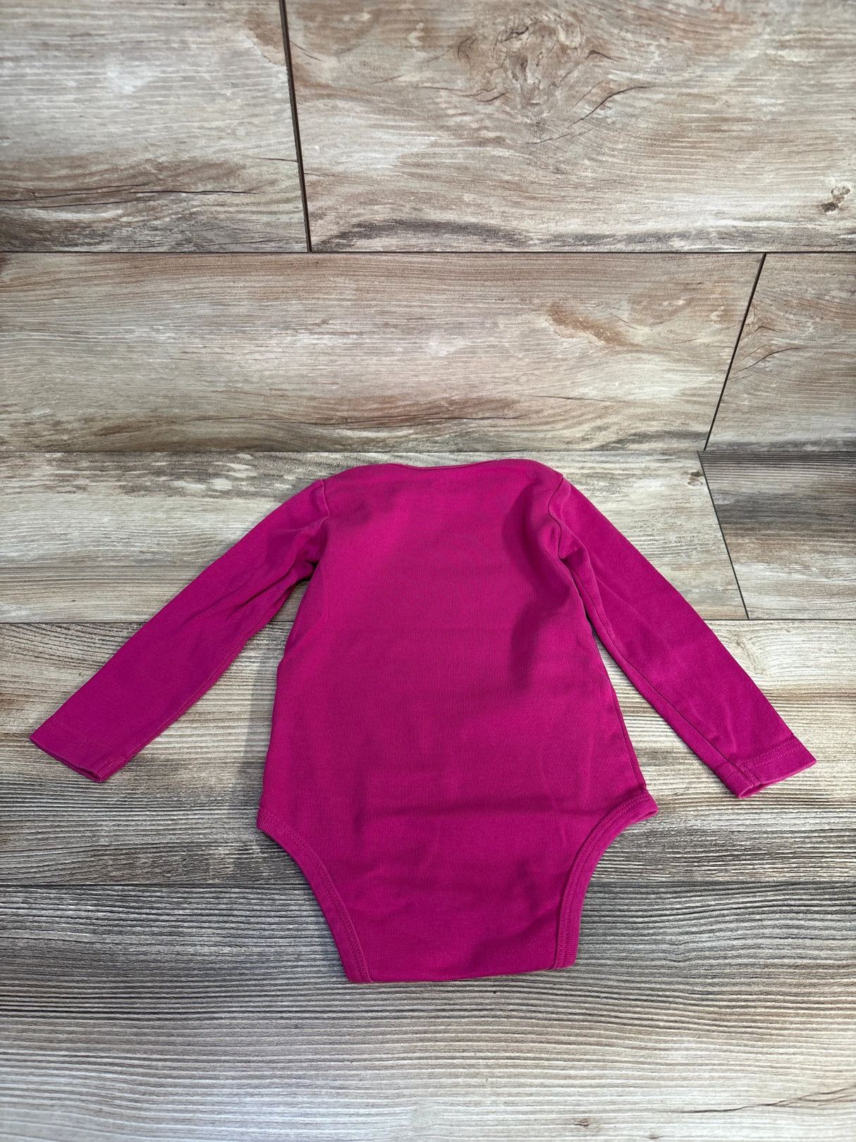 Back view of Primary long sleeve bodysuit in hot pink showing long sleeves and snap crotch on wooden background