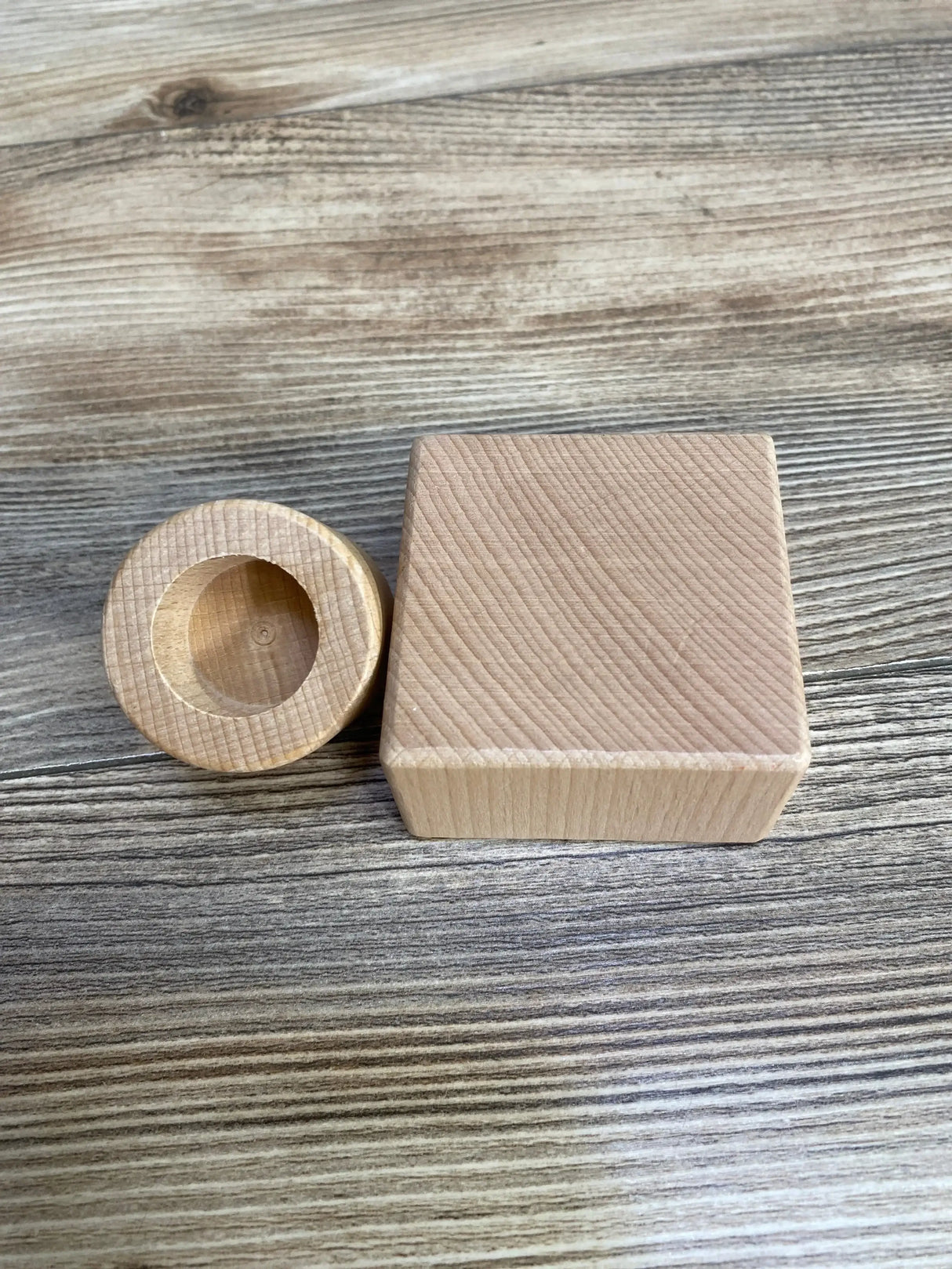 Top view of Lovevery Pincer Puzzle wooden square block and round cup piece showing natural wood grain on wood tabletop