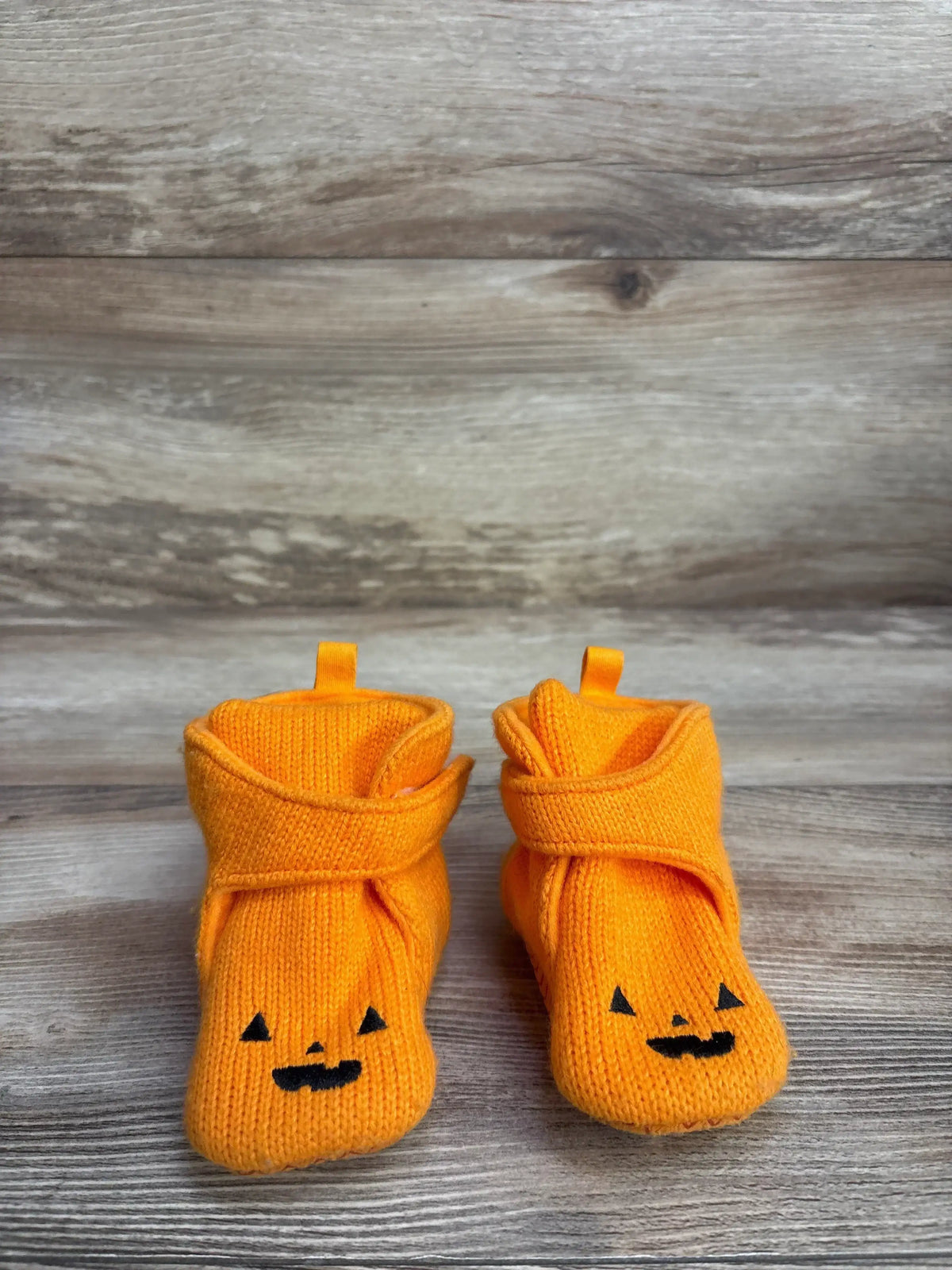 Orange knit baby booties with jack-o'-lantern faces on wooden background