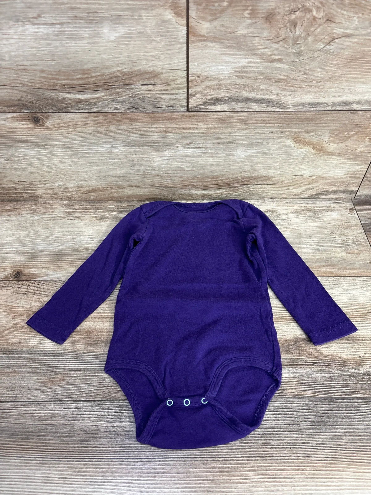 Purple long sleeve baby bodysuit on wood floor, infant clothing flat lay