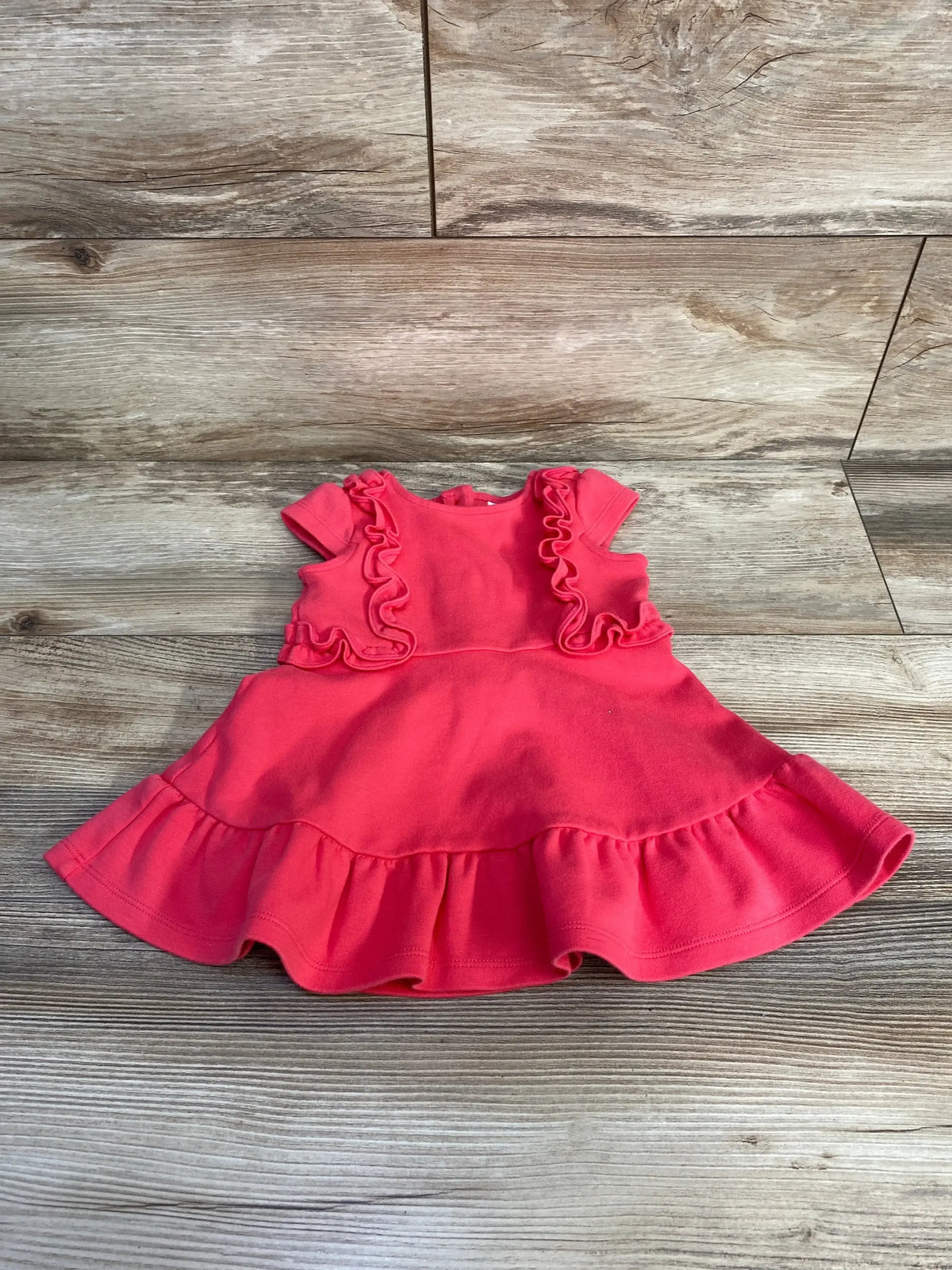 Flat lay of pink Janie and Jack baby ruffle dress showing ruffled bodice, cap sleeves, and ruffled hem on wood floor
