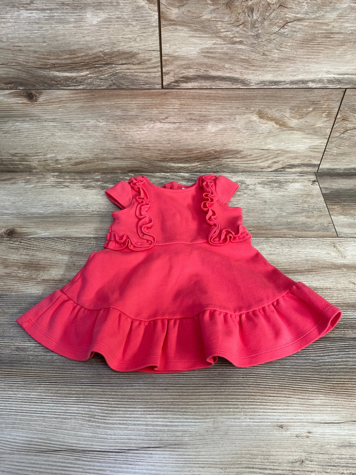 Flat lay of pink Janie and Jack baby ruffle dress showing ruffled bodice, cap sleeves, and ruffled hem on wood floor