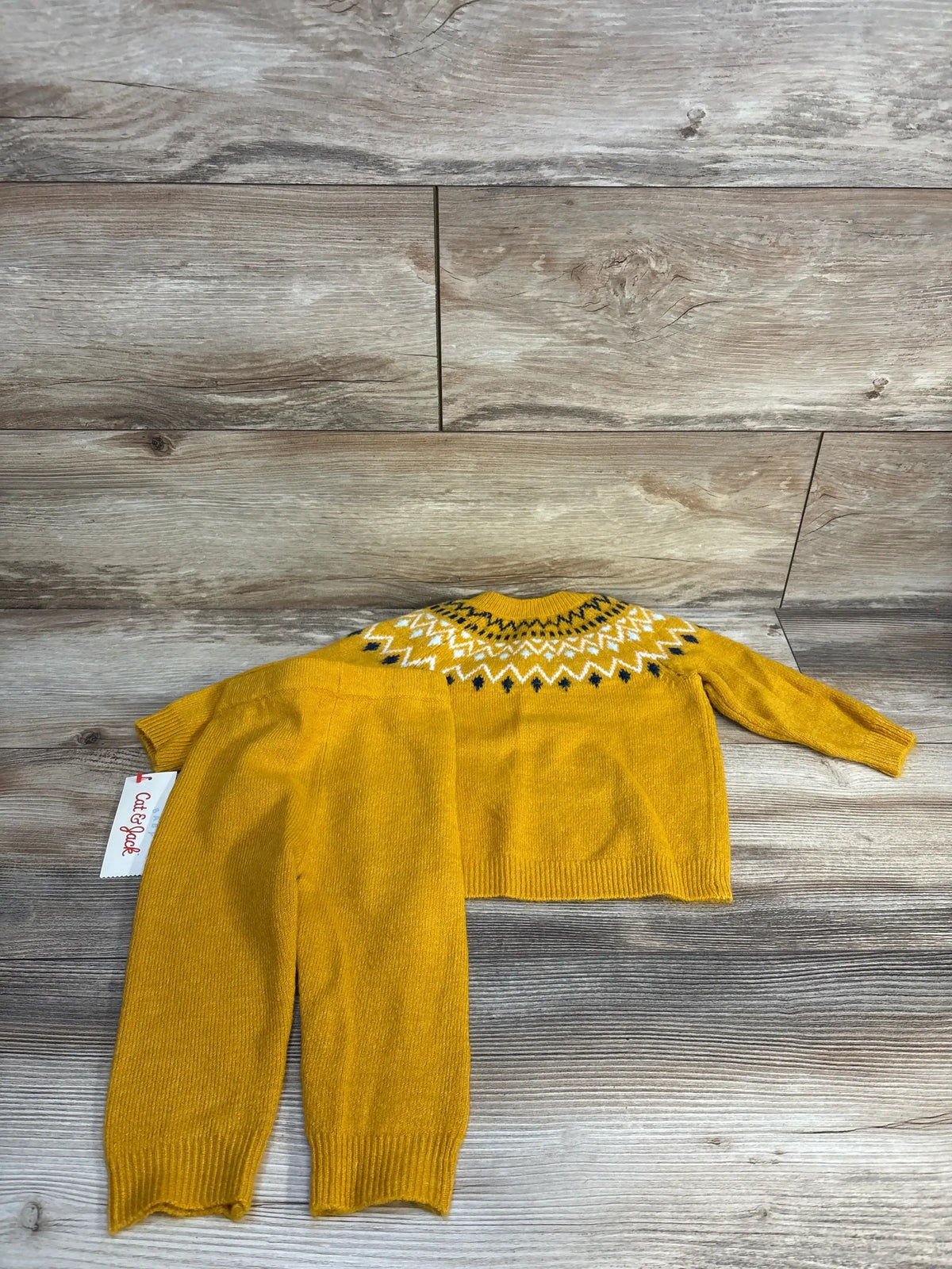 Yellow knit baby sweater and pants set with patterned neckline on wood floor