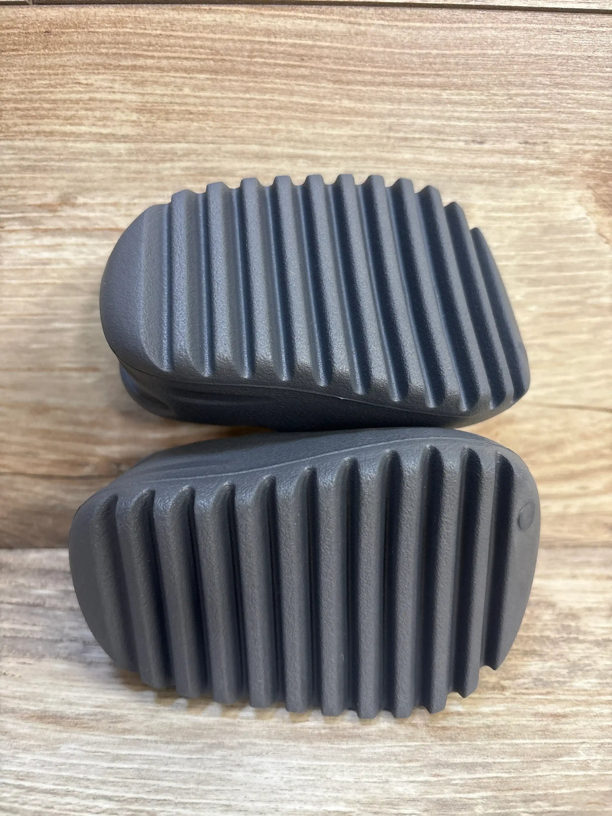 Top view of Adidas Yeezy Slides in Granit size 3C showing ribbed outsoles on wood background