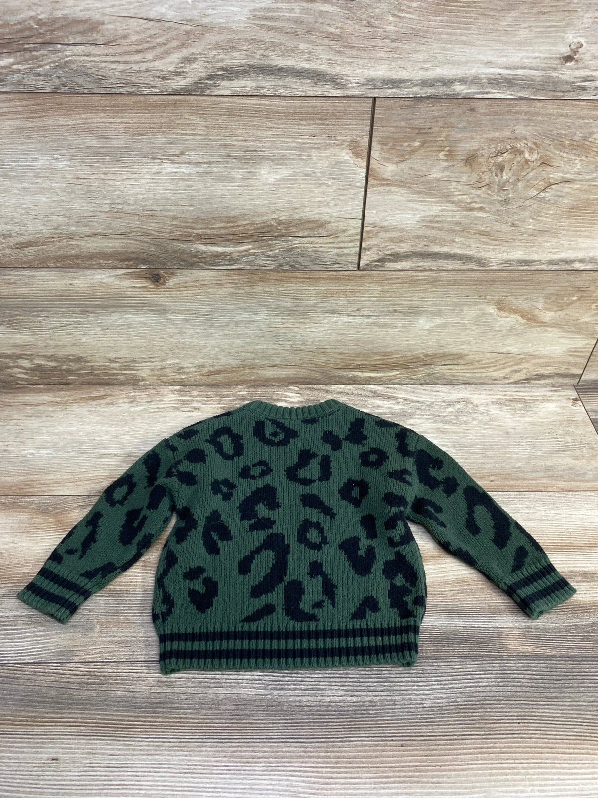 Green knit kids sweater with black leopard print pattern on wooden floor