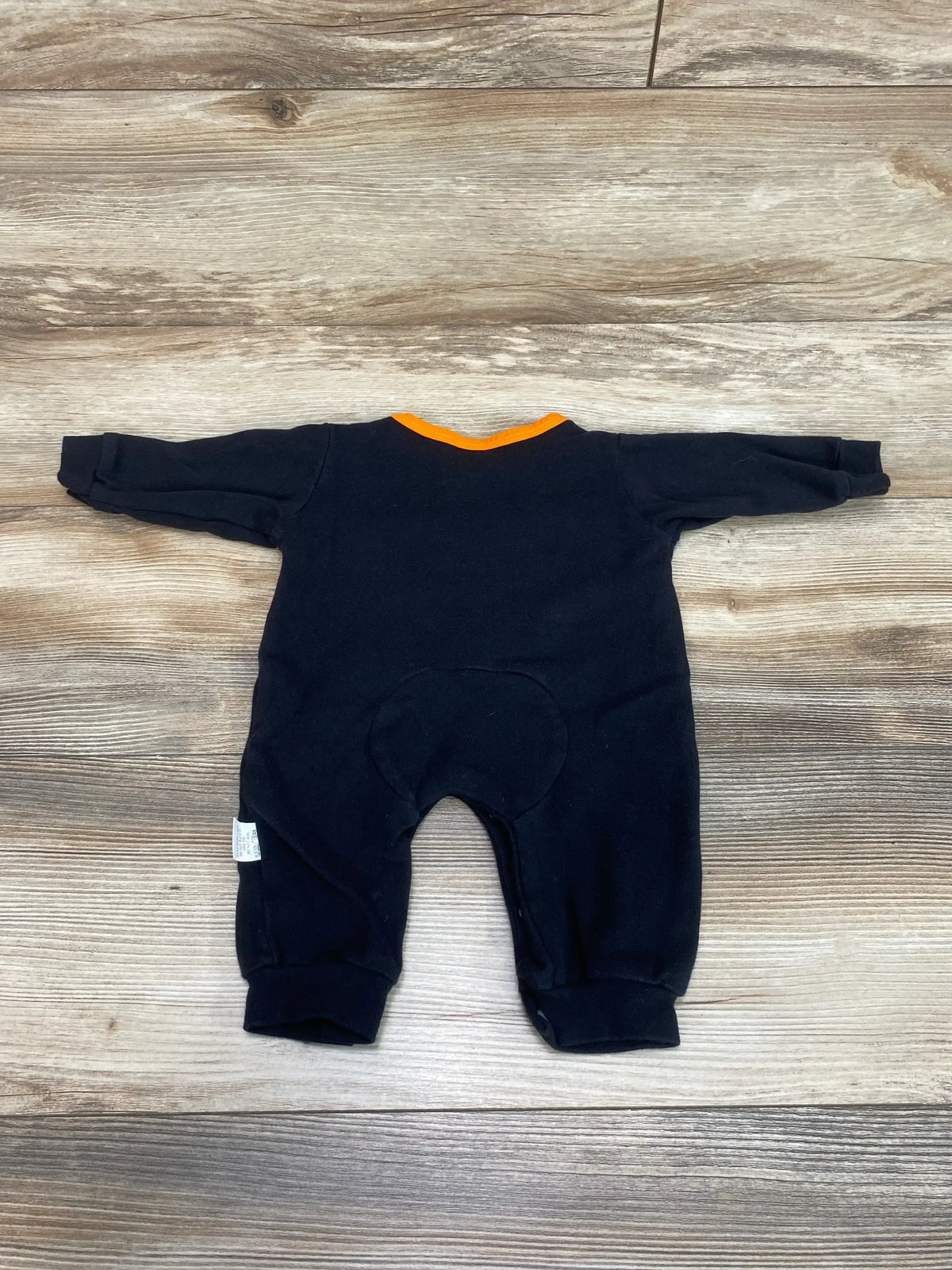 Back flat lay of black baby coverall (3M) showing orange neckline and seat patch on wood background