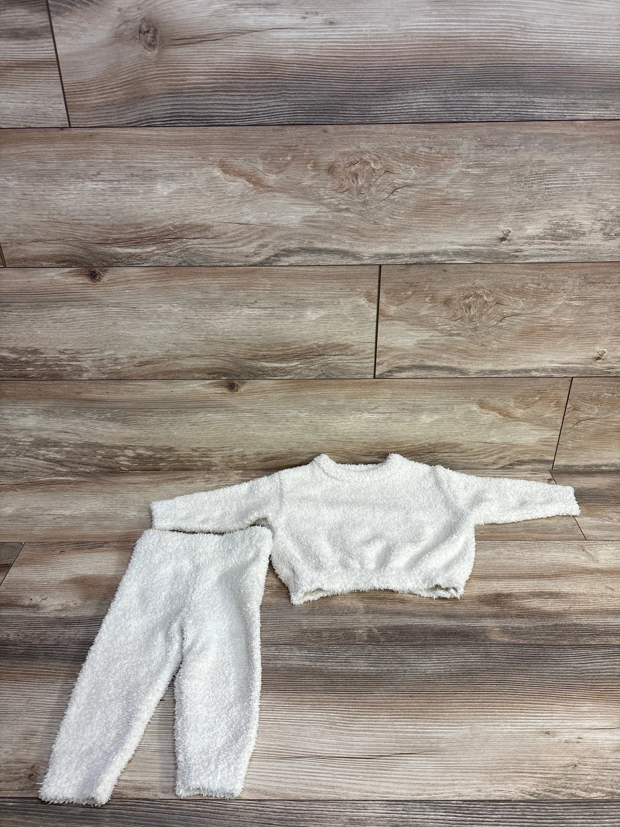 White fuzzy long-sleeve crop top and matching high-waisted pants children’s outfit laid flat on wood floor