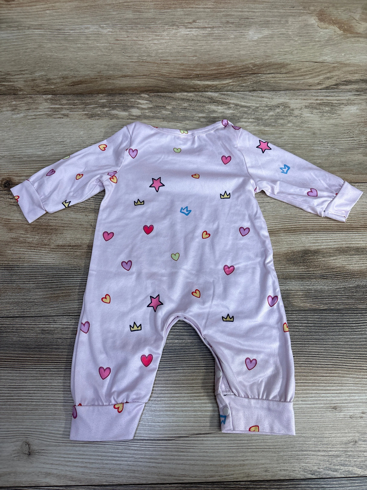 Light pink baby romper with heart, star, and crown prints on wooden surface