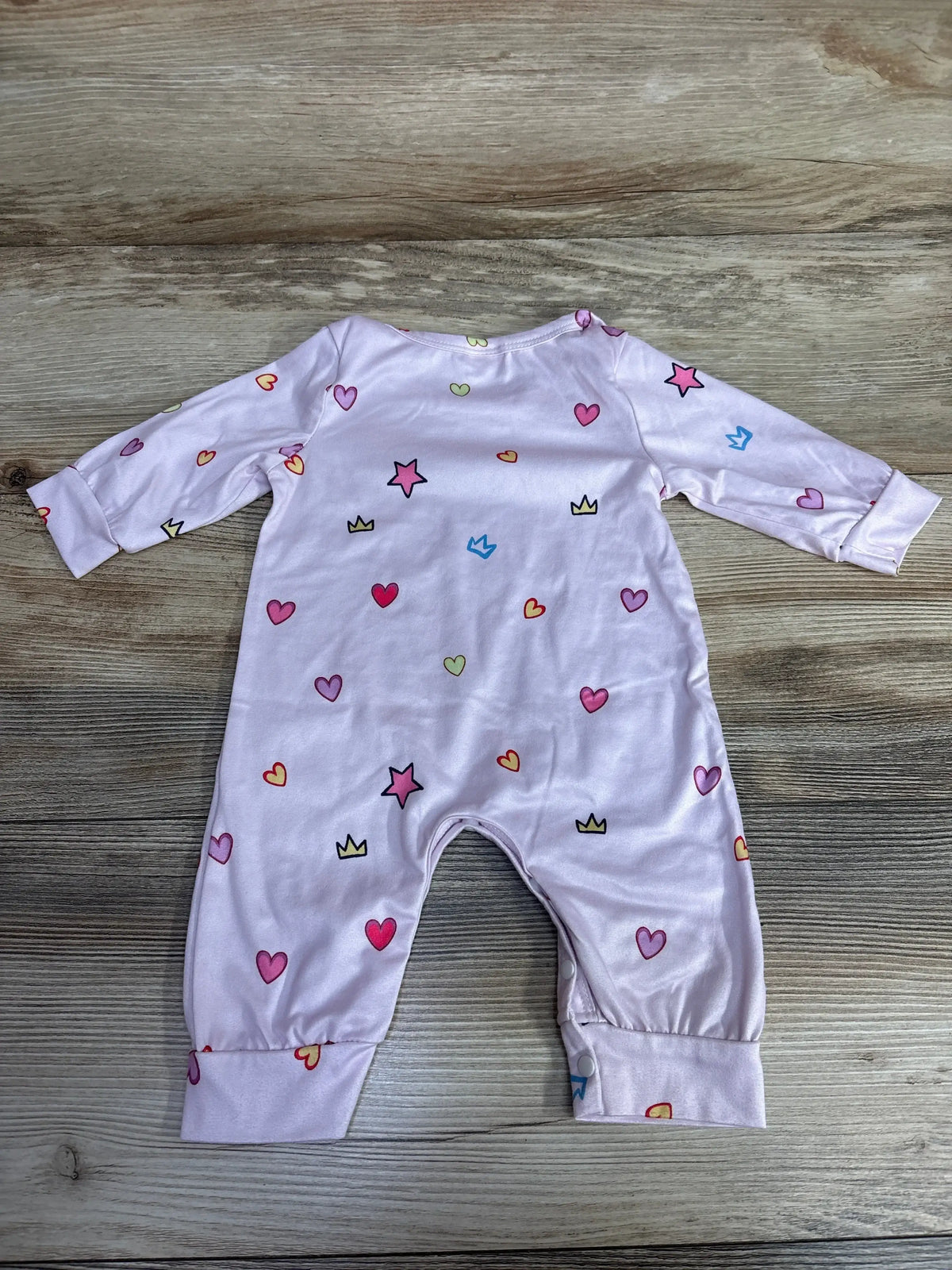 Back flat lay of newborn pink coverall size 1-3m with multicolored hearts, stars, crowns and leg snaps on wooden background