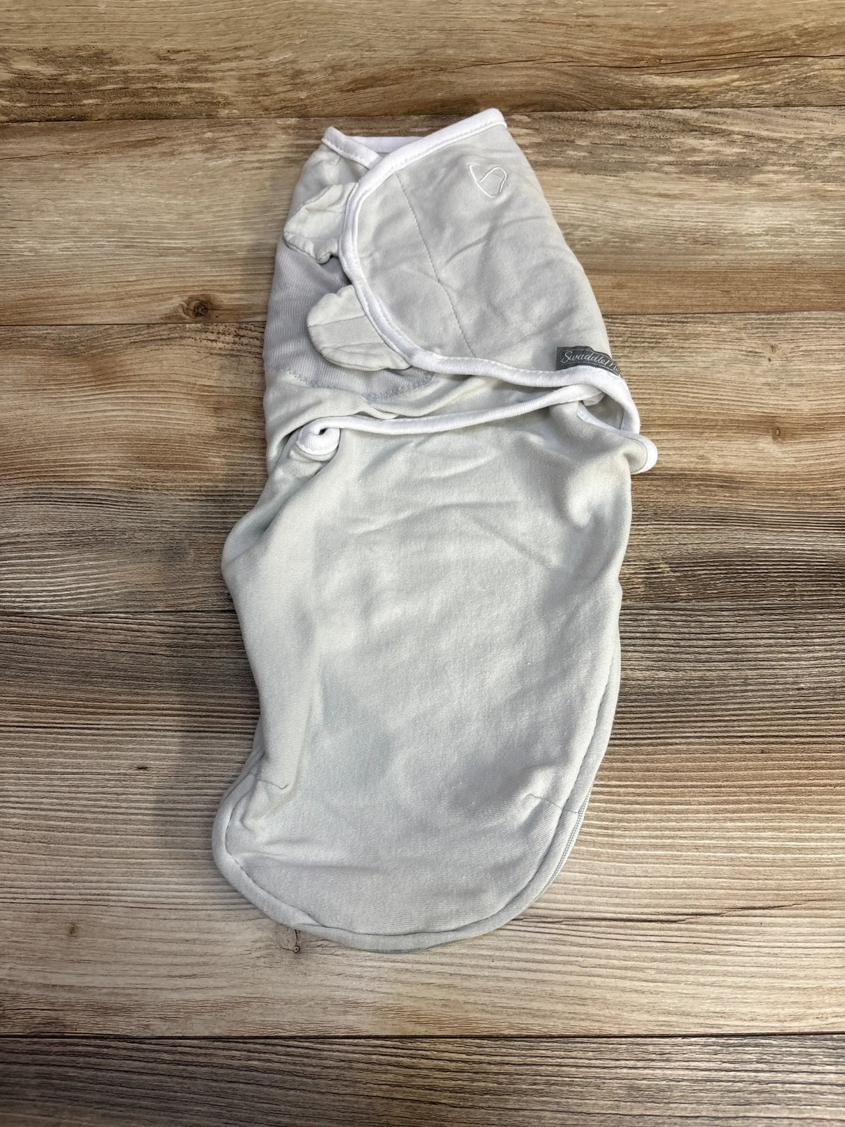 Top view of SwaddleMe grey swaddle (0-3 months) with Velcro wing closures and embroidered heart on wood