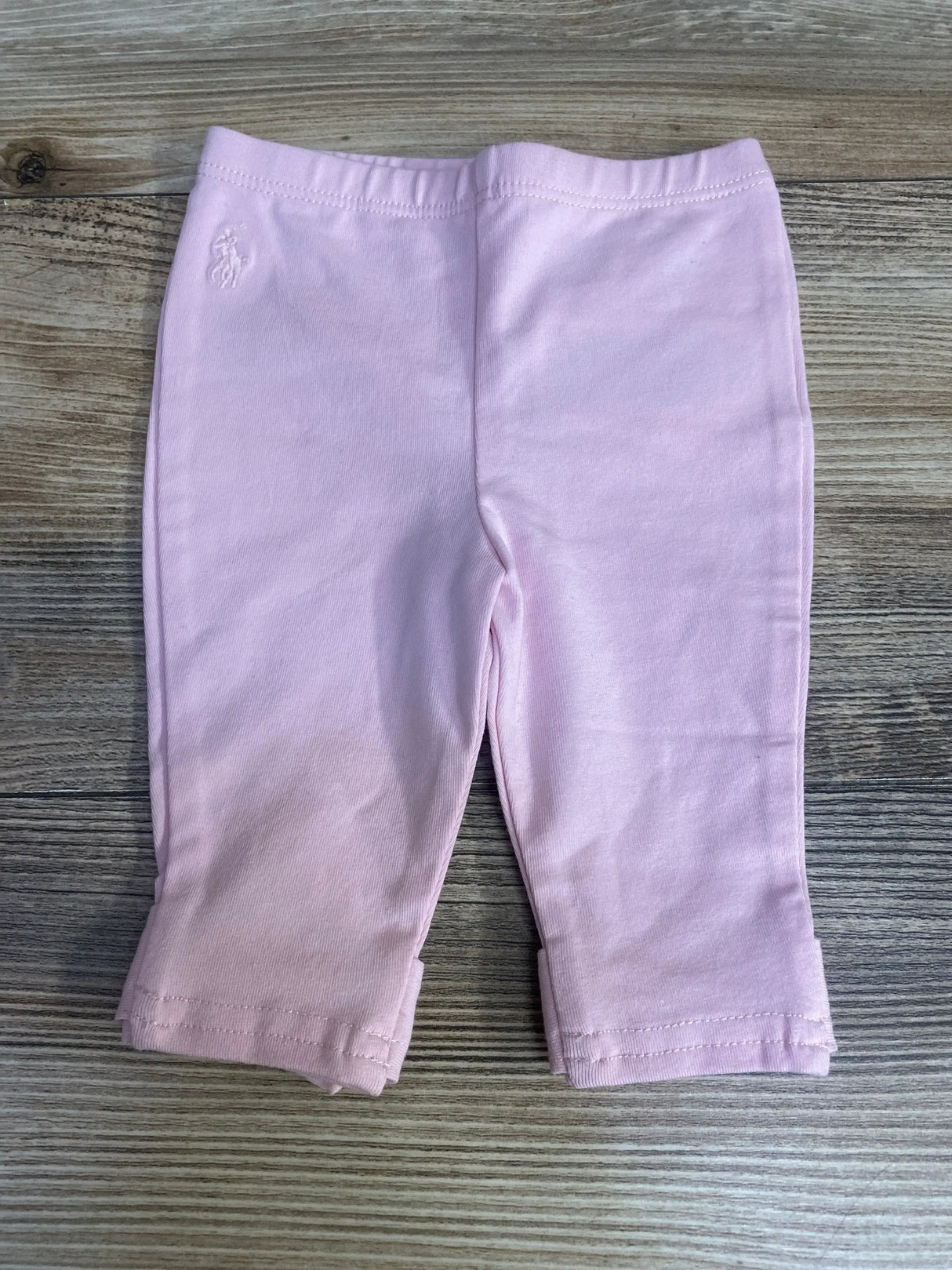 Flat-lay of pink Ralph Lauren baby leggings with elastic waist, embroidered pony at hip, folded cuffs on wood background