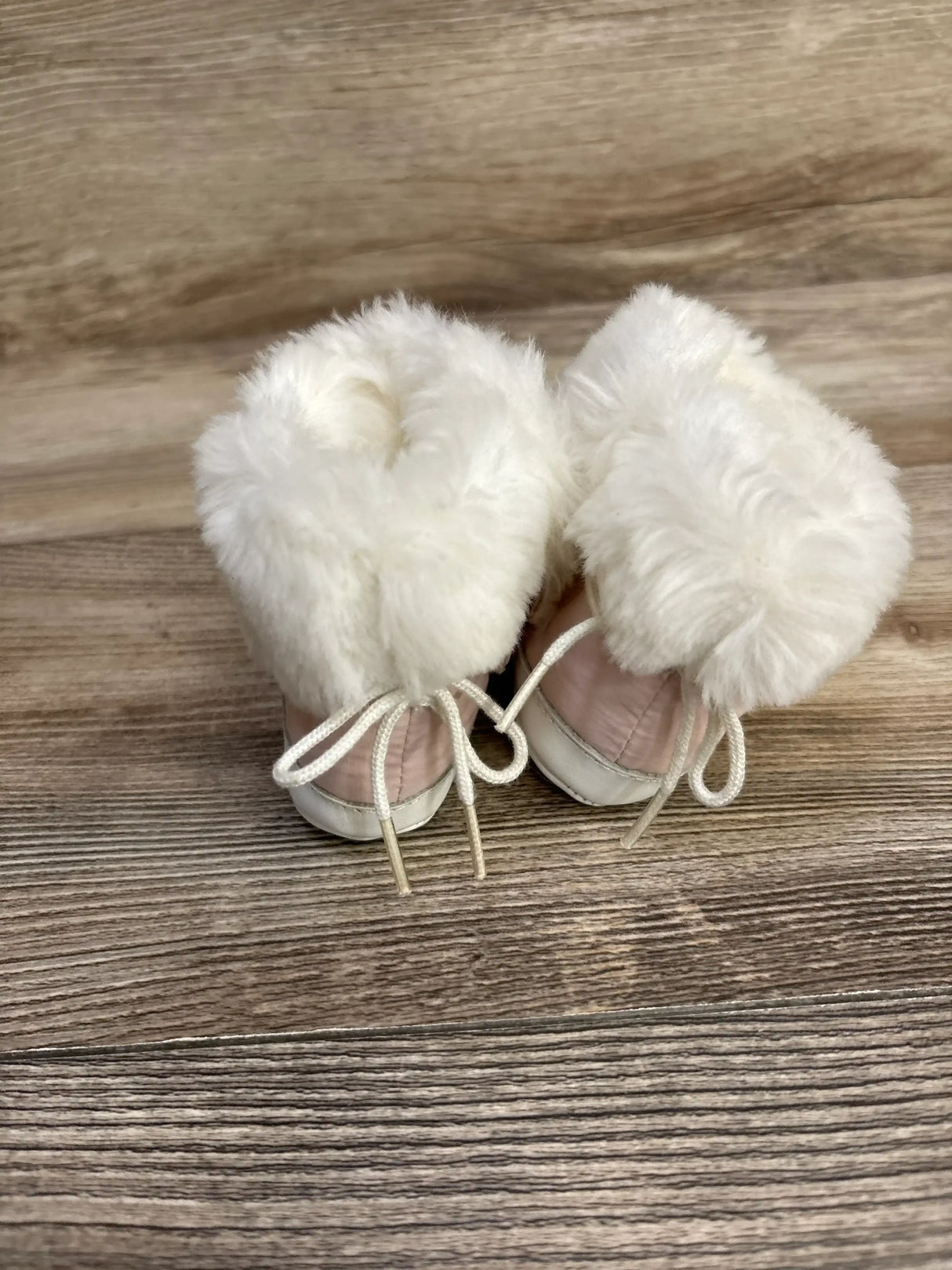 Pair of pink baby boots with white faux fur trim on wooden floor