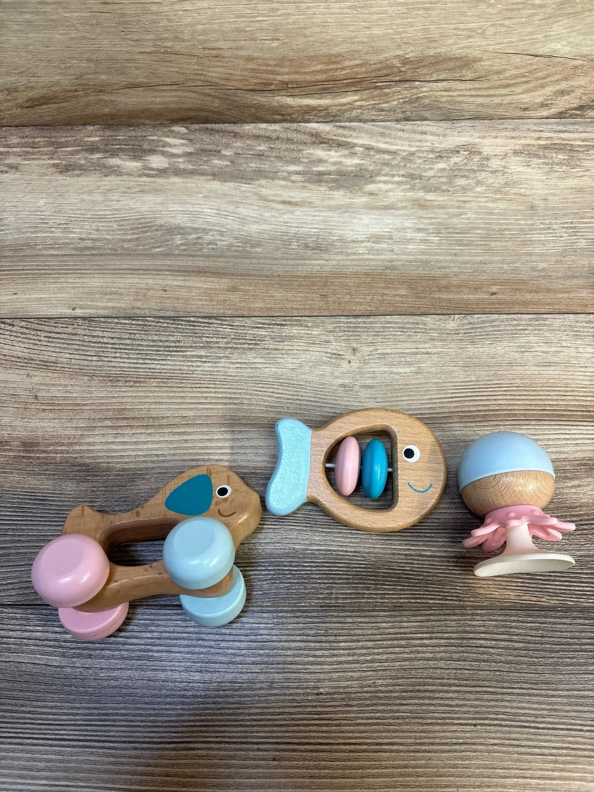 Top-down view of Hape Multi Sensory Wooden Toys 3pk showcasing fish rattle, stay put rattle, and dog on wheels on a wood surface