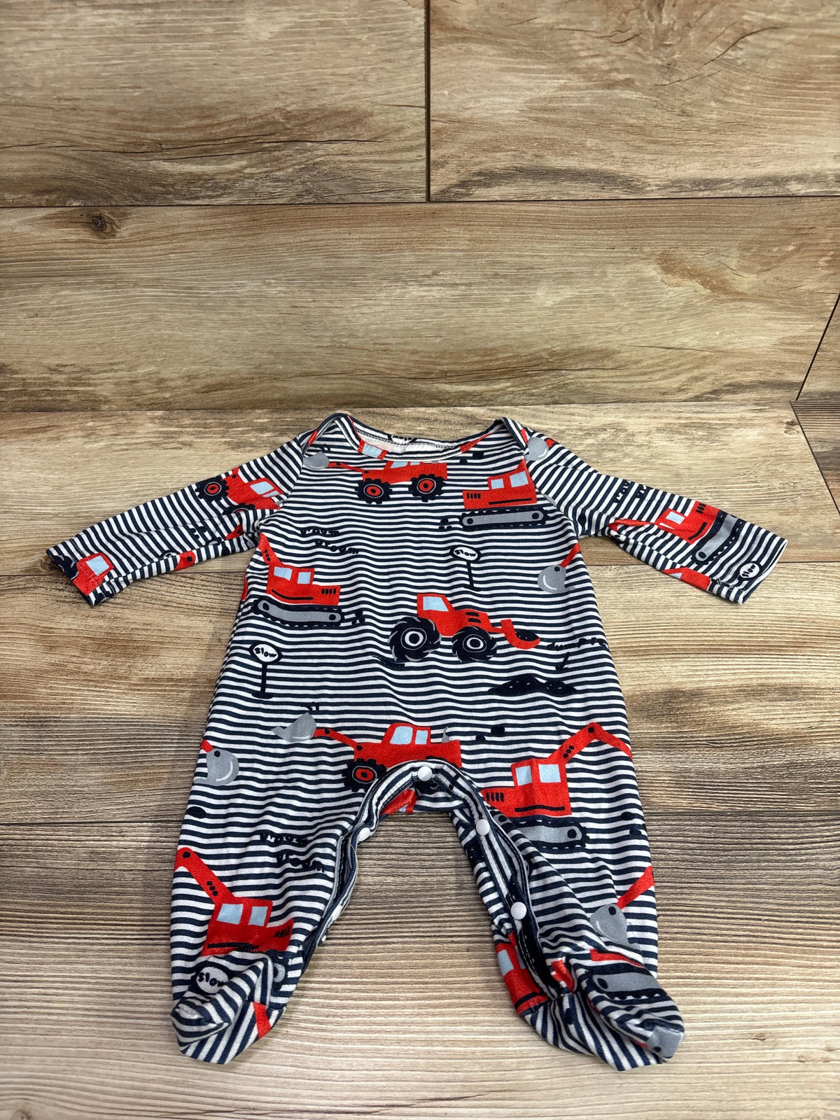 Front view of a navy tractor print footed coverall in size 1 to 3 months on a wooden floor