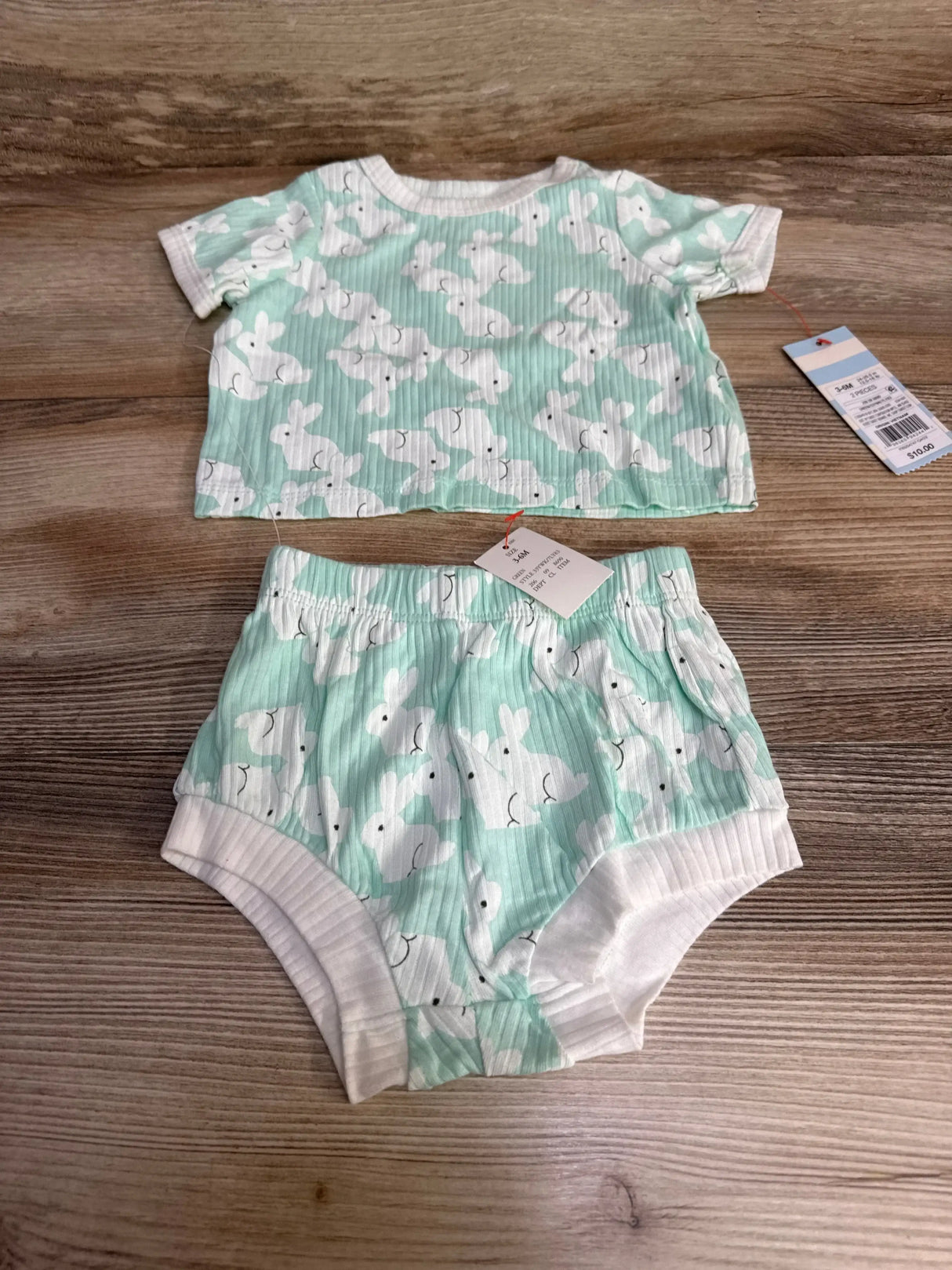 Flat lay of Cat & Jack mint two-piece baby set showing ribbed short-sleeve top and elastic-waist bunny-print shorts on wood