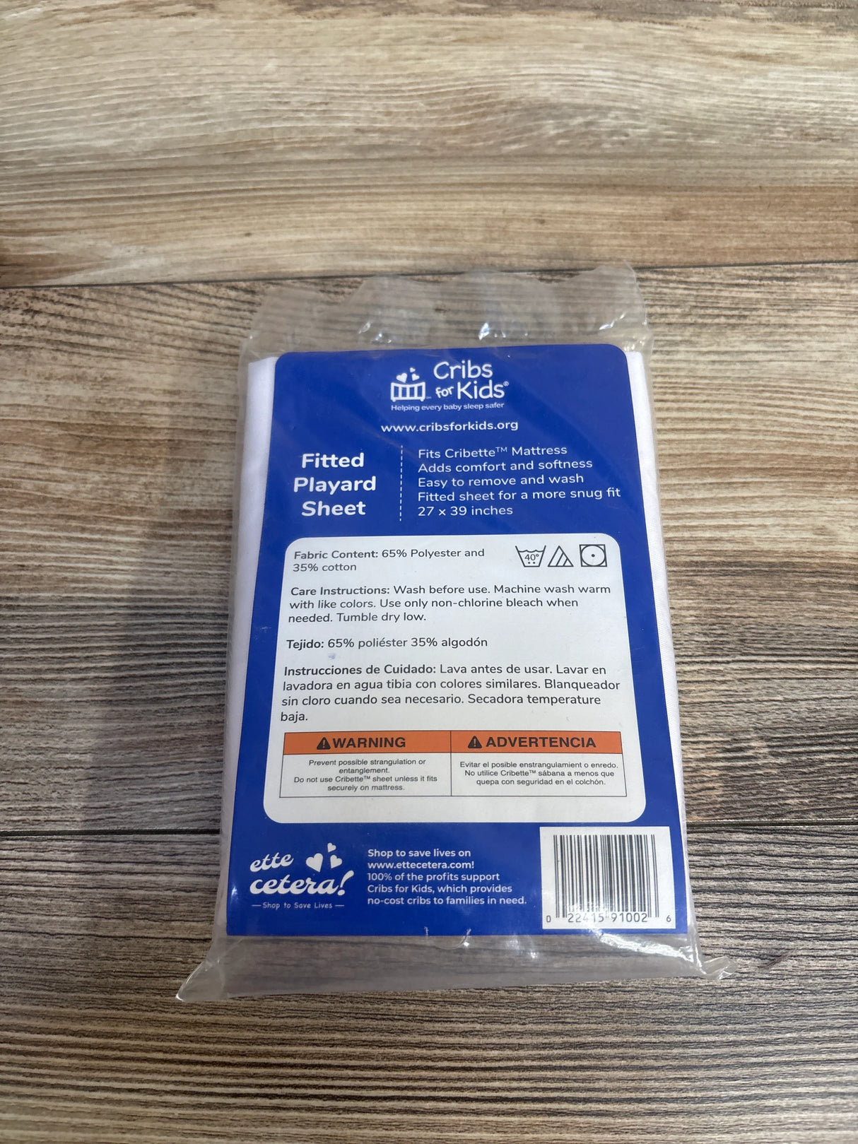 Cribs for Kids fitted playard sheet in packaging on wooden surface, blue and white label visible.