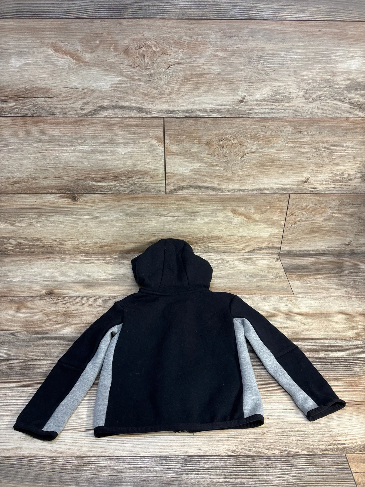 Black kids hoodie with gray sleeve panels, laid flat on wood floor