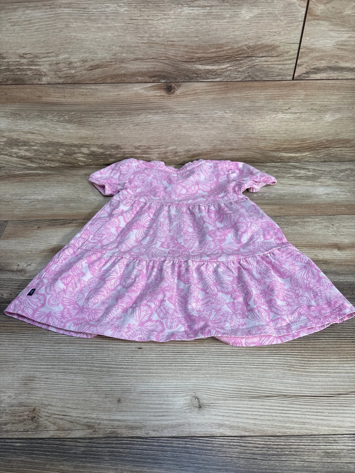 Top-down view of Gap Kids pink 3T dress with butterfly print, short sleeves and tiered skirt on wood background