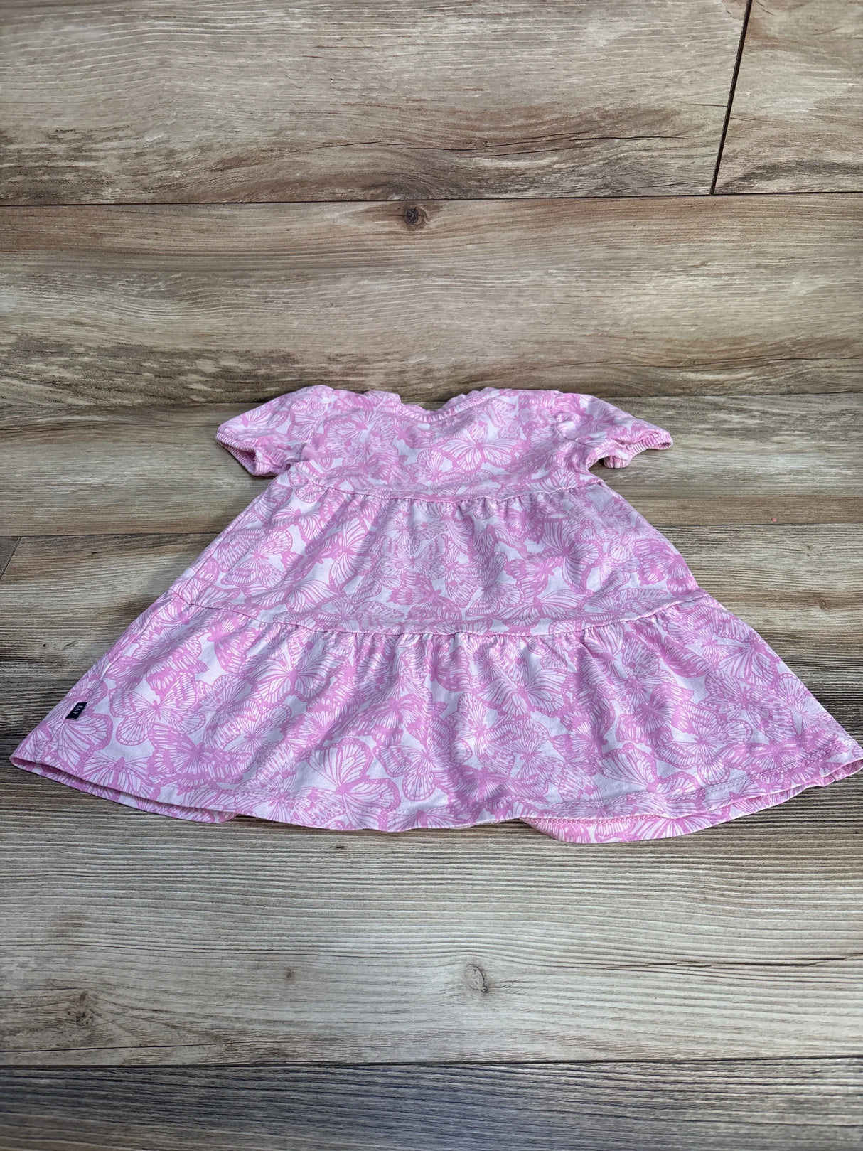 Top-down view of Gap Kids pink 3T dress with butterfly print, short sleeves and tiered skirt on wood background