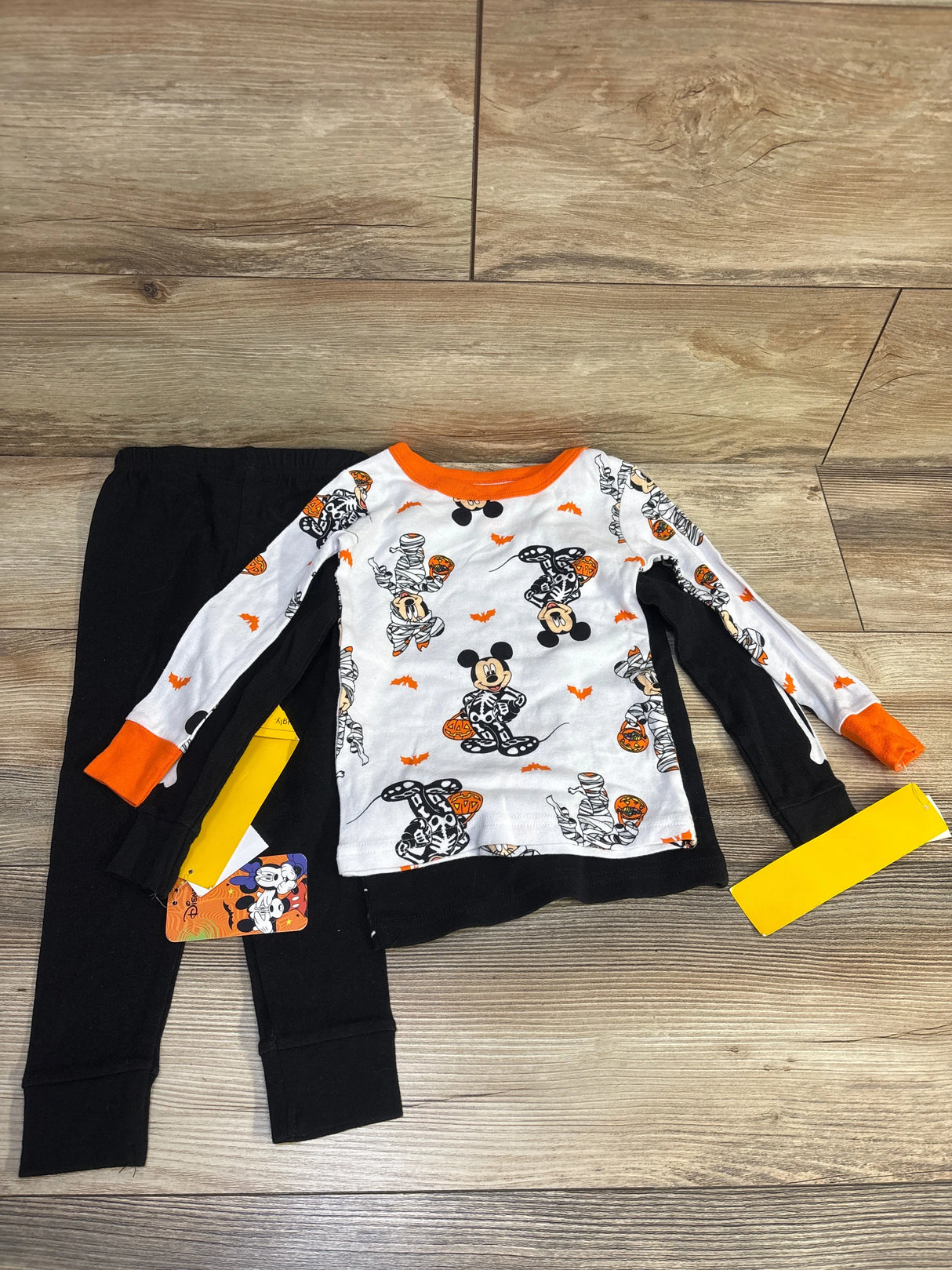 Flat lay of Disney Mickey Mouse Halloween pajamas: white top with Mickey print and orange cuffs, black pants on wood floor
