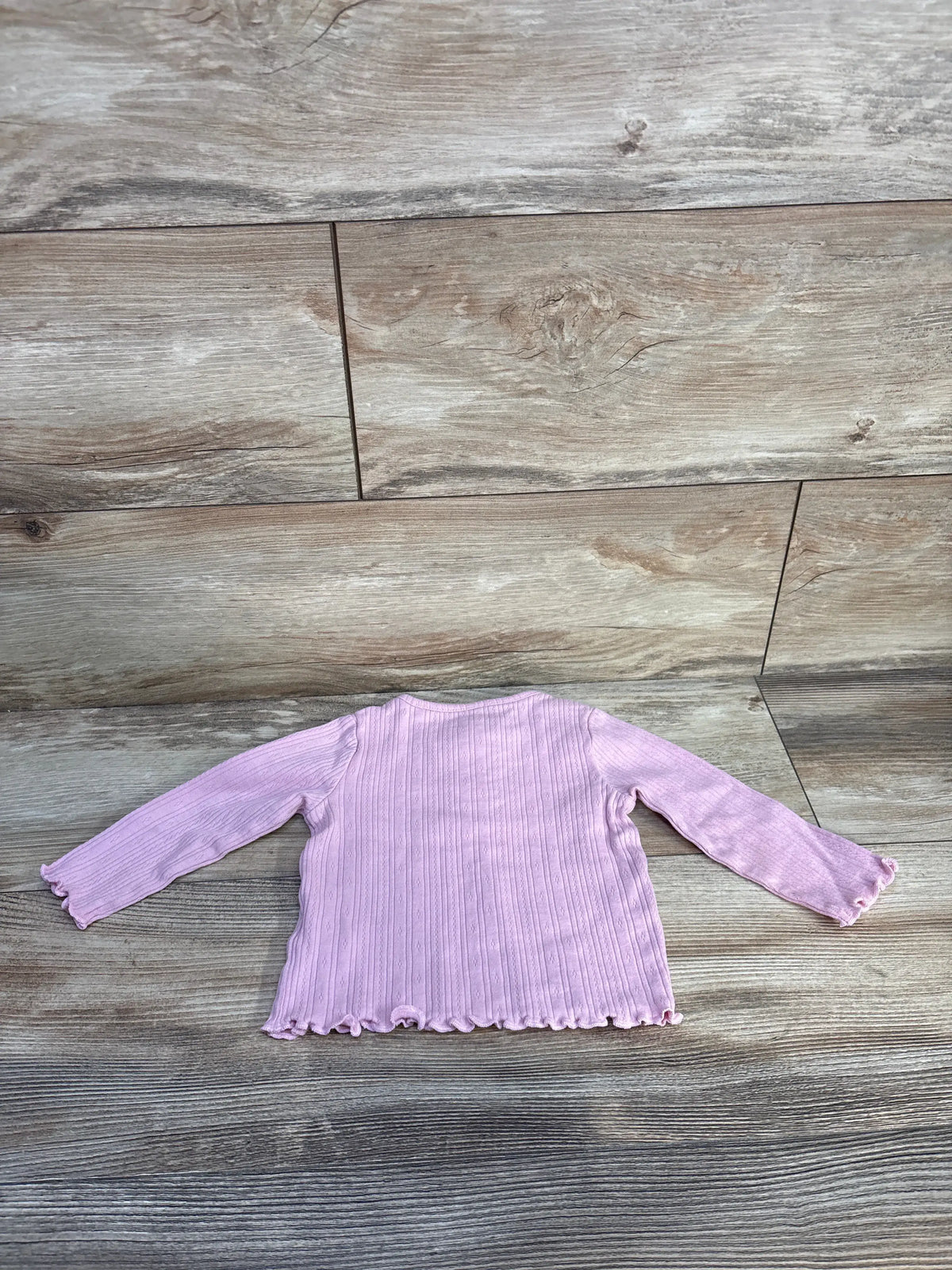 Overhead view of Topomini pink ribbed henley shirt in size 3 to 6 months, showcasing long sleeves and ribbed fabric on wood