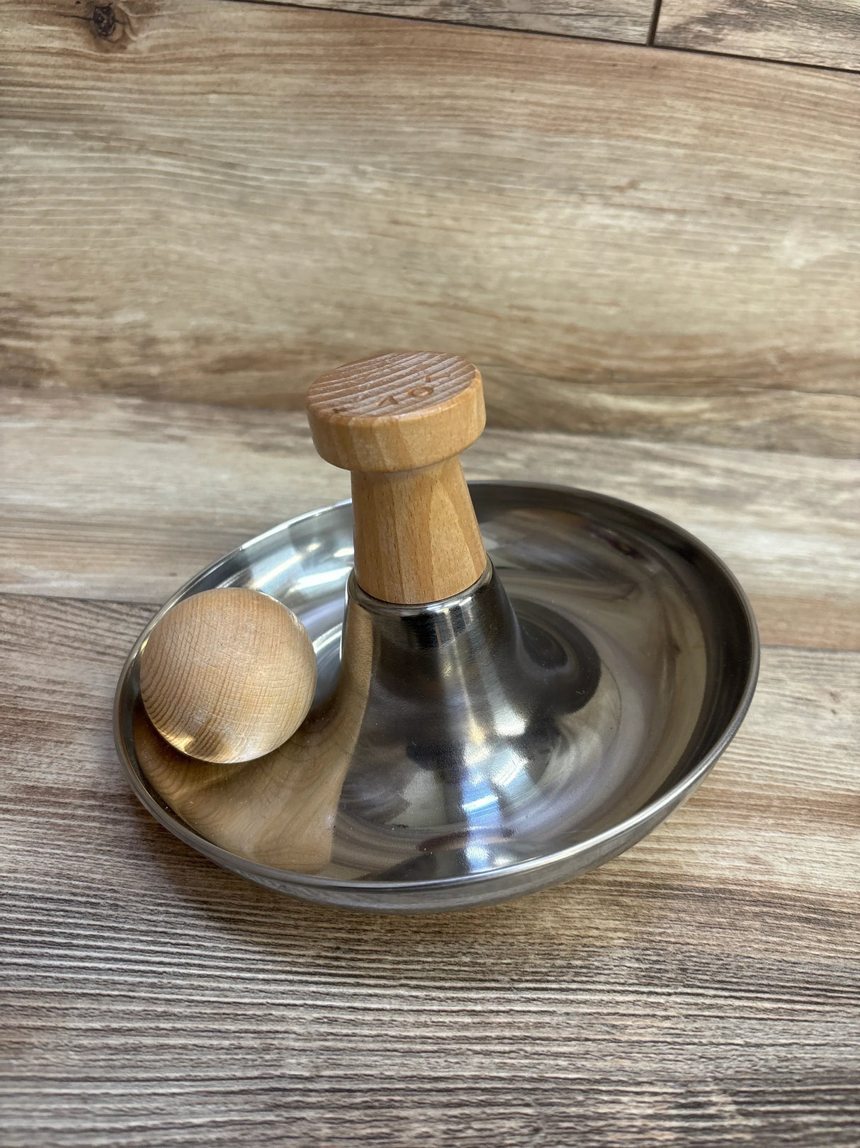 Angled view of Lovevery Stainless Steel Tip & Turn with stainless steel base, wooden handle and tamper ball on wood surface