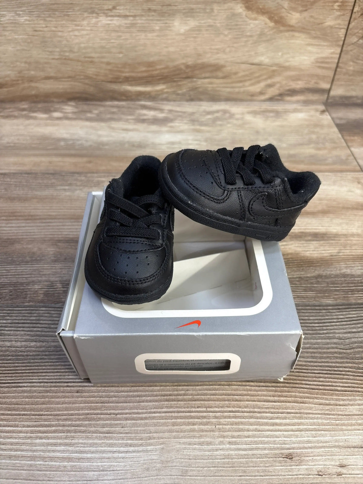 Front and side views of black Nike Air Force 1 crib shoes, size 1C, showing perforated toes and Nike Swoosh on a shoebox
