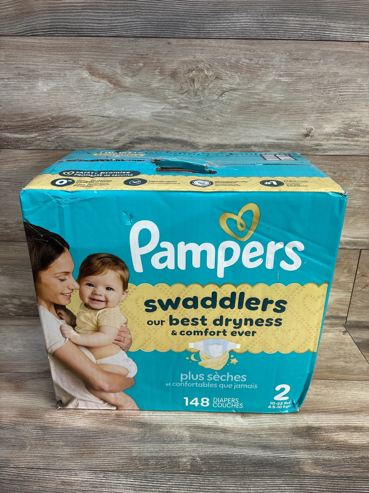 Front of Pampers Swaddlers size 2 box, ‘our best dryness and comfort ever’ text, 148-count, baby in parent’s arms on wood