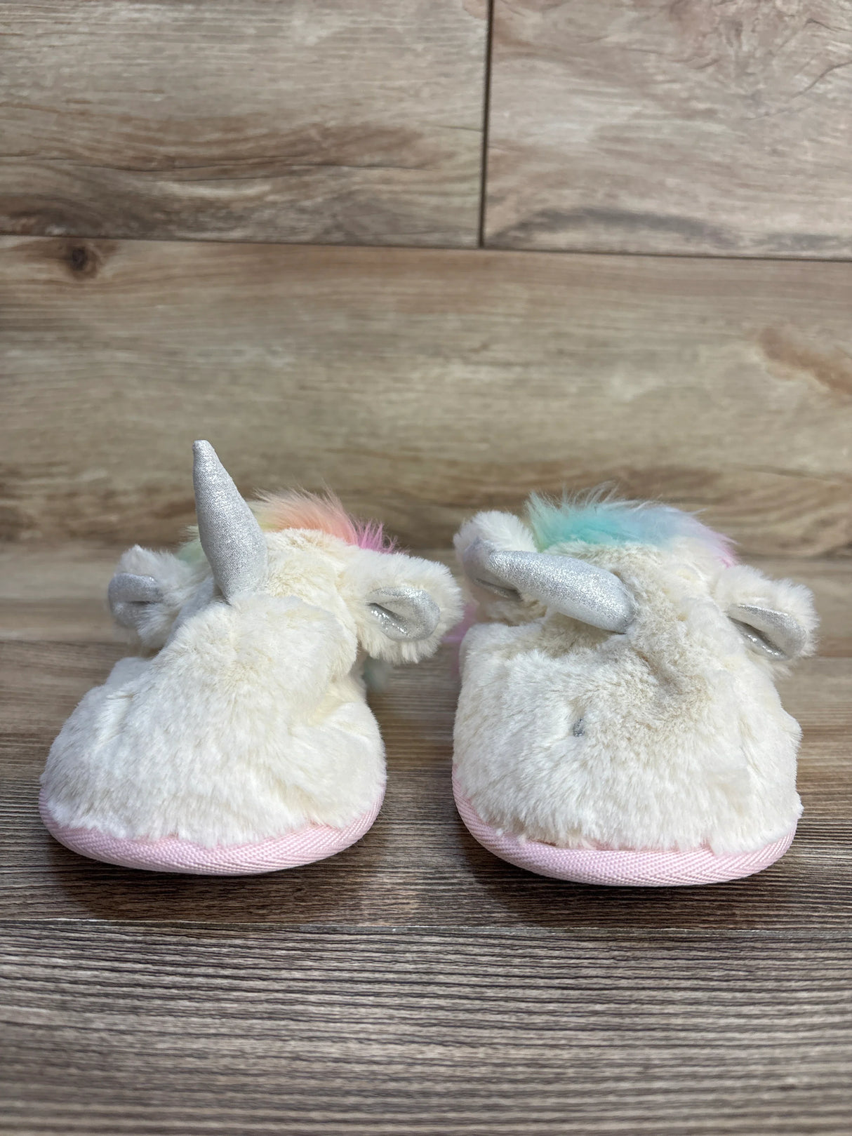 Soft unicorn baby booties with rainbow mane, silver horn, and pink soles on wood floor
