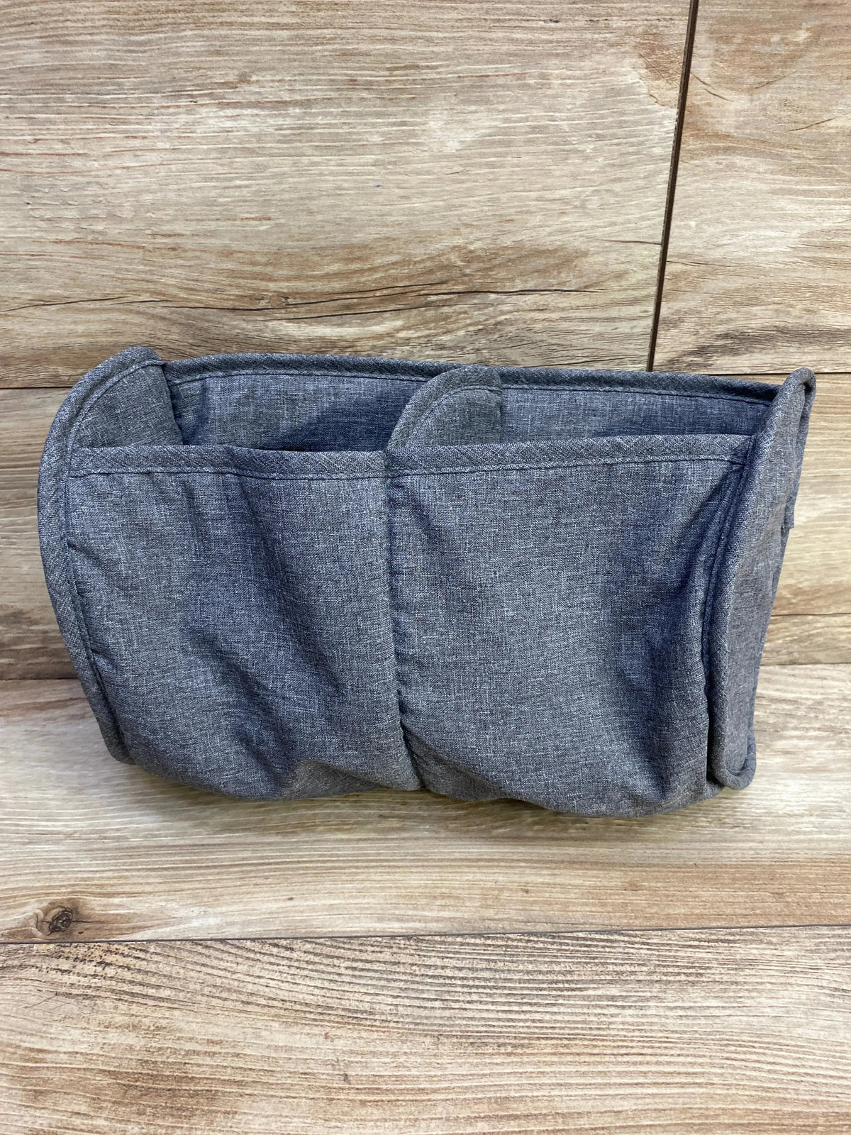 Front view of grey fabric playard organizer showing three pockets and padded sides on wooden backdrop