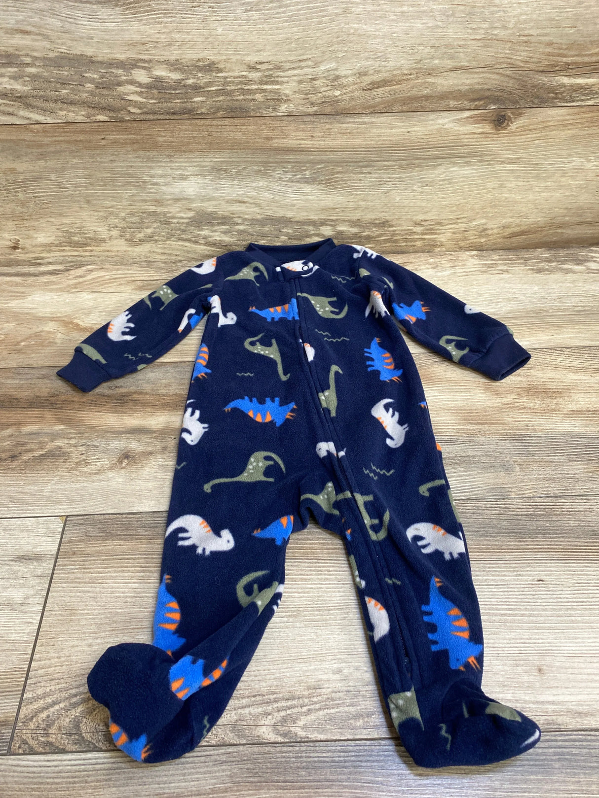 Navy blue baby sleeper with colorful dinosaur print and zipper, displayed on wood floor