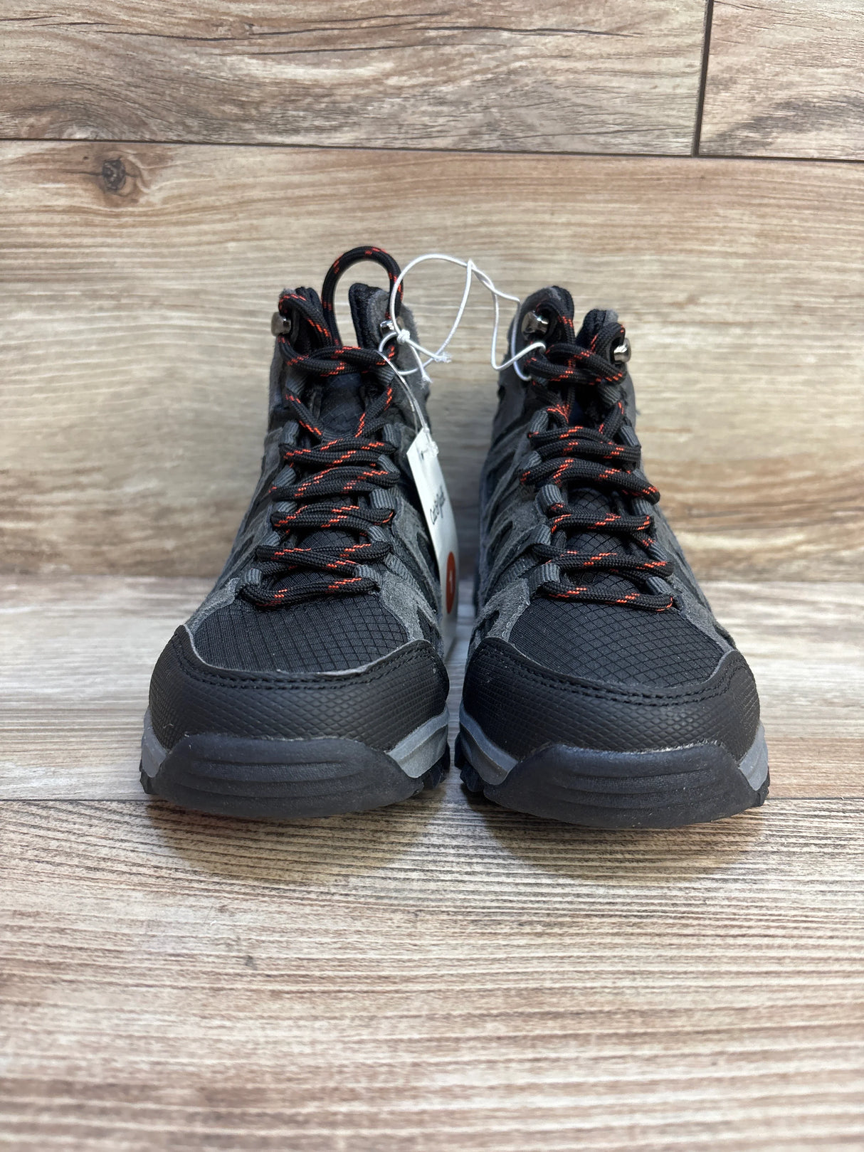 Front view of black and gray kids hiking shoes with red laces on wooden floor