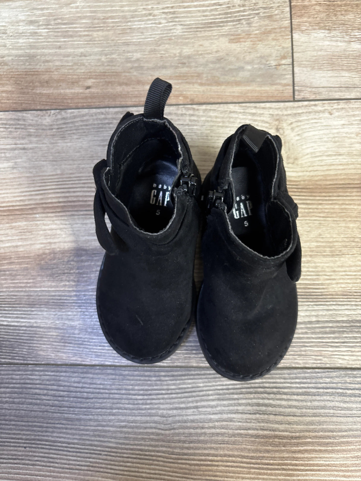 Top-down view of Baby Gap bow ankle boots showcasing bow detail, side zippers, and size 5 printed inside on light wood floor