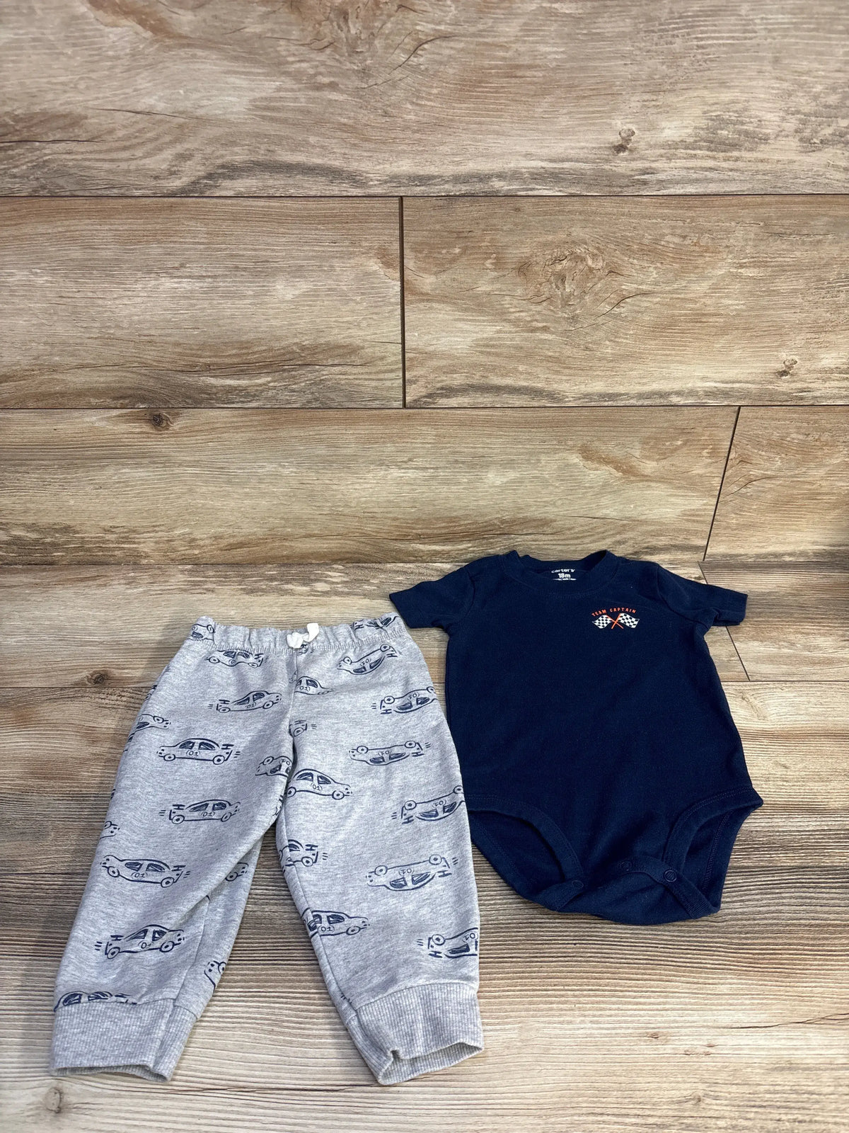 Top view of Carter’s navy bodysuit and shorts set showcasing Team Captain chest graphic and patterned gray bottoms on wood floor