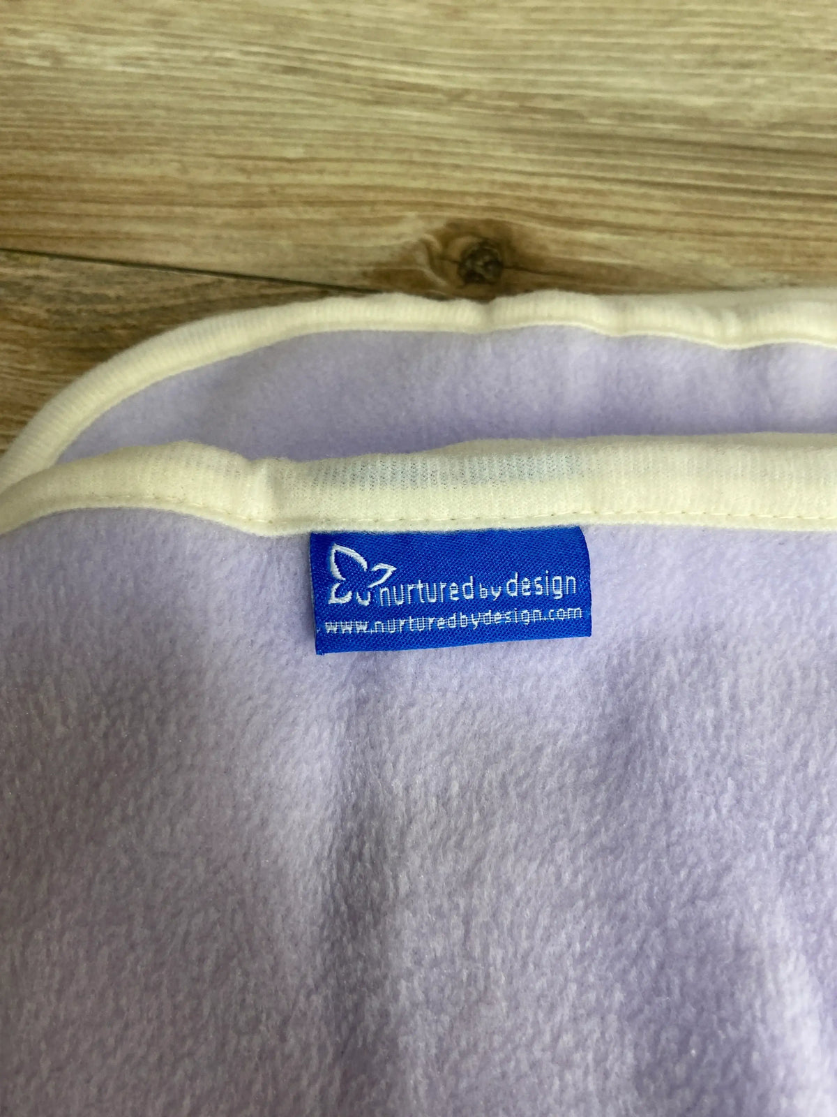 Close-up of a soft lavender fleece baby blanket with a nurtured by design label on wood surface