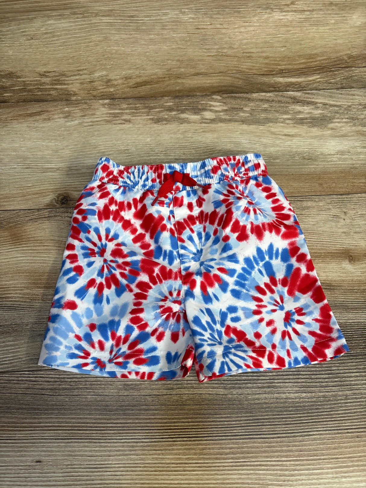 Red, white, and blue tie-dye kids swim trunks with drawstring waist on wood floor