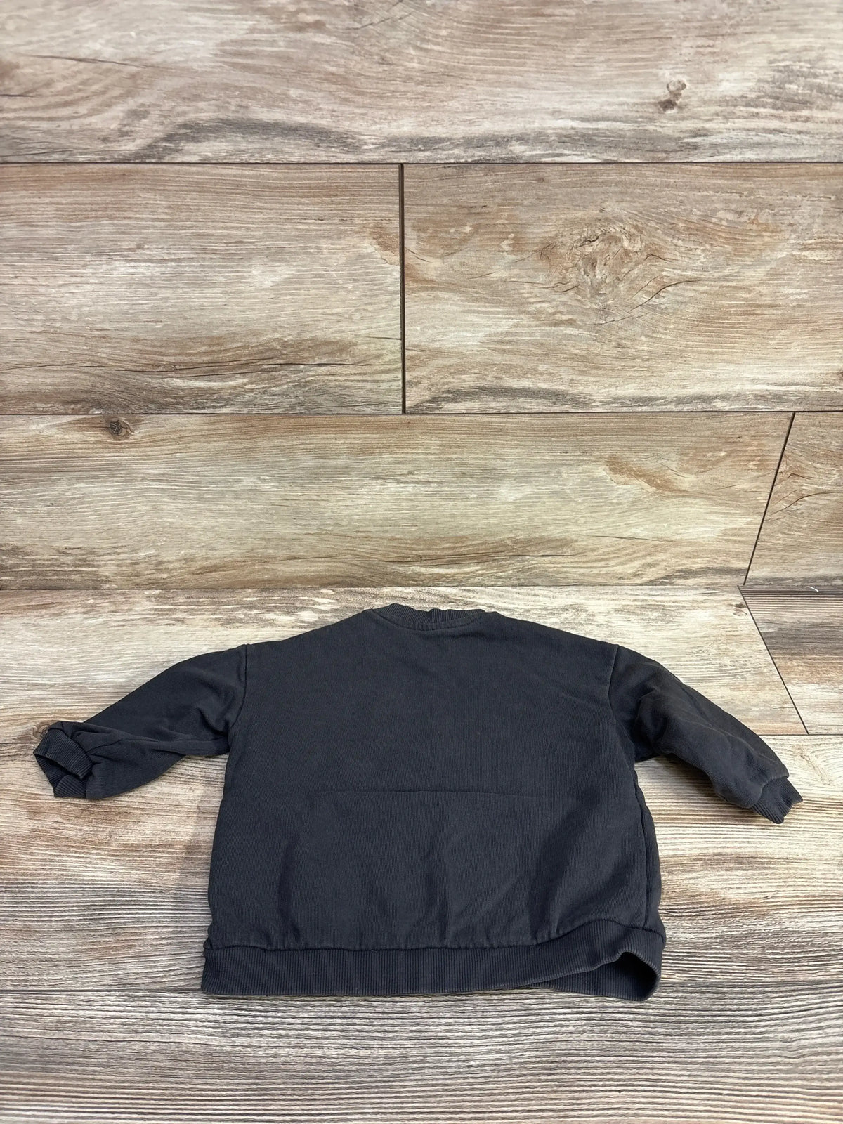 Back view of H&M toddler crewneck sweatshirt in grey, size 12 months, showing ribbed cuffs and hem on wood-textured floor