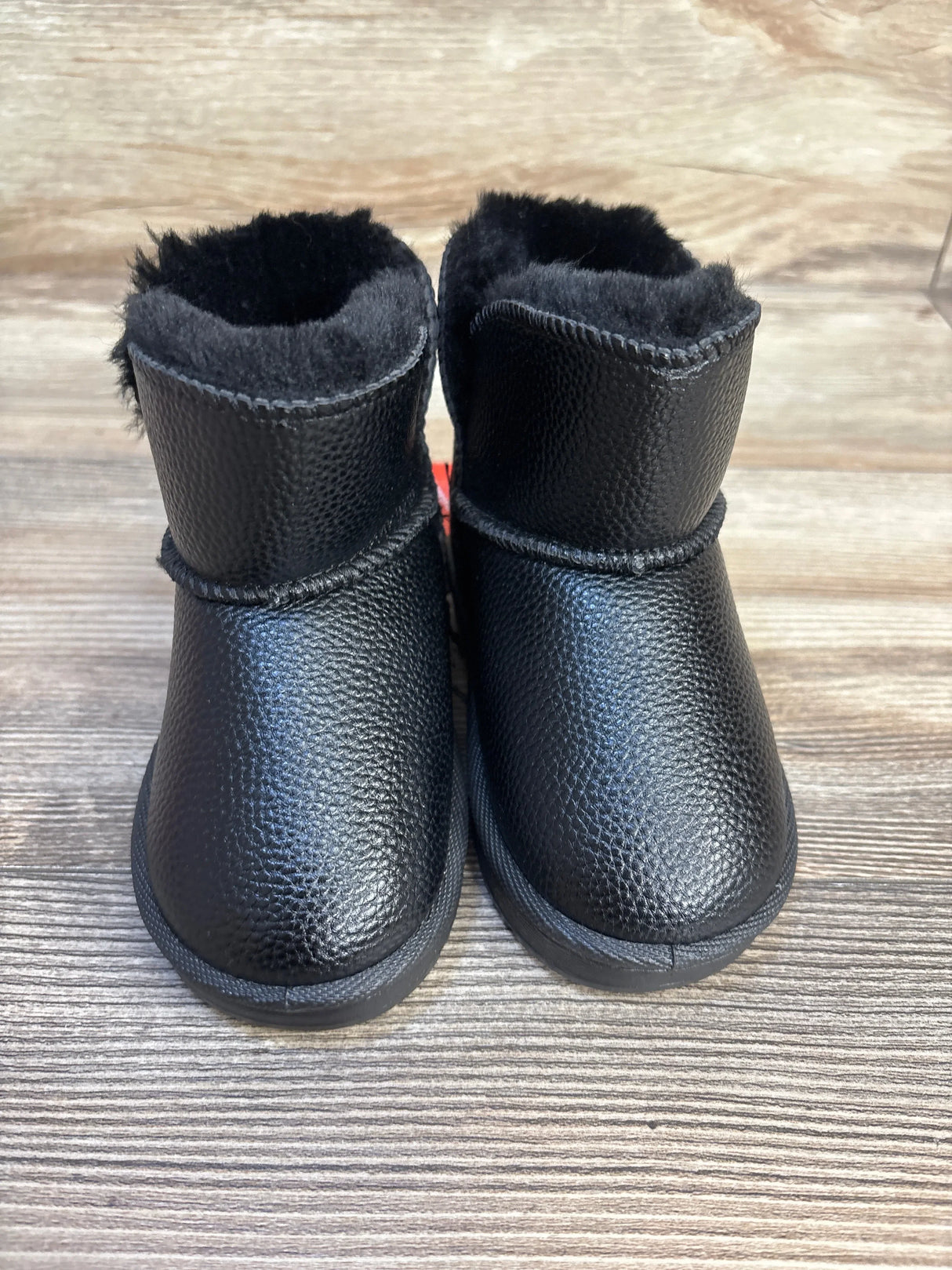 Black faux leather toddler boots with fuzzy lining on wood background