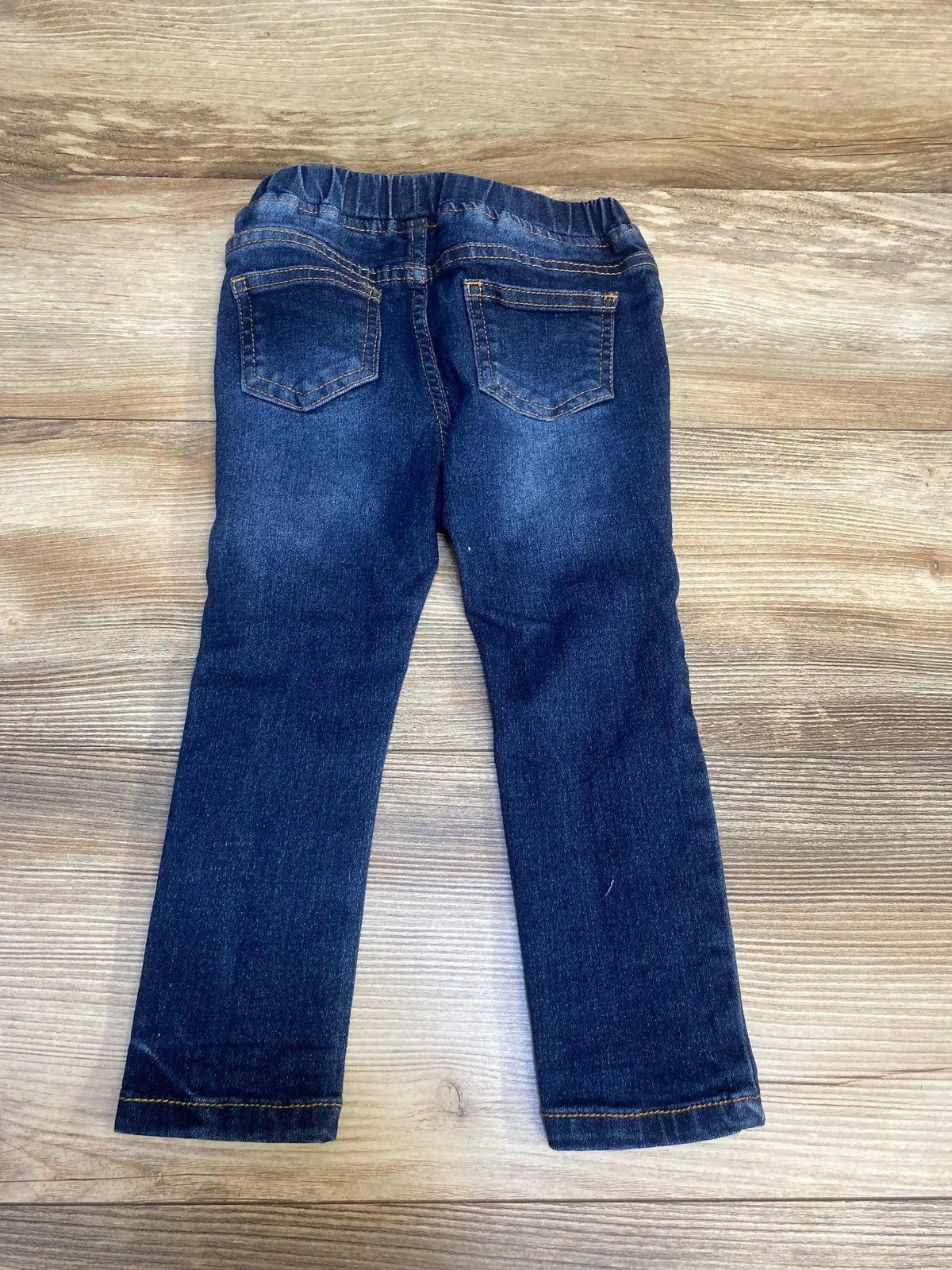 Dark wash kids jeans with elastic waistband and back pockets on wood background