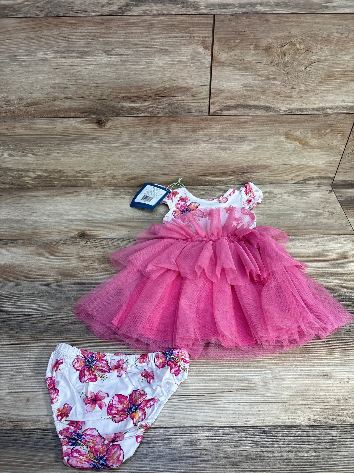 Front flat lay of Coco Moon pink tutu dress and floral bloomers, layered tulle skirt and floral bodice on wood background