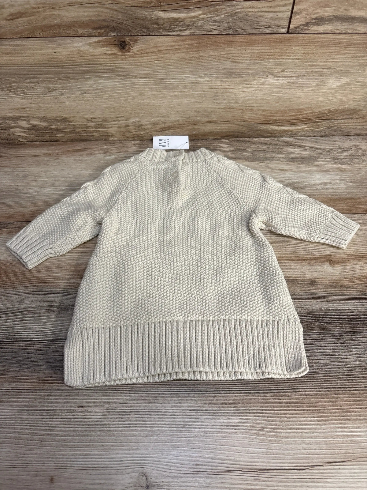 Flat lay of Baby Gap beige cable knit sweater dress (3-6 months) showing textured stitch, ribbed hem and long sleeves on wood background