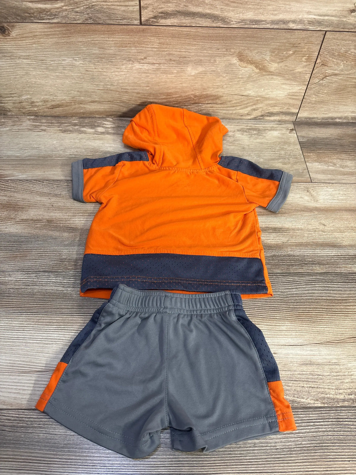 Flat lay of orange hooded toddler shirt with gray perforated trim and matching gray elastic shorts on wood background