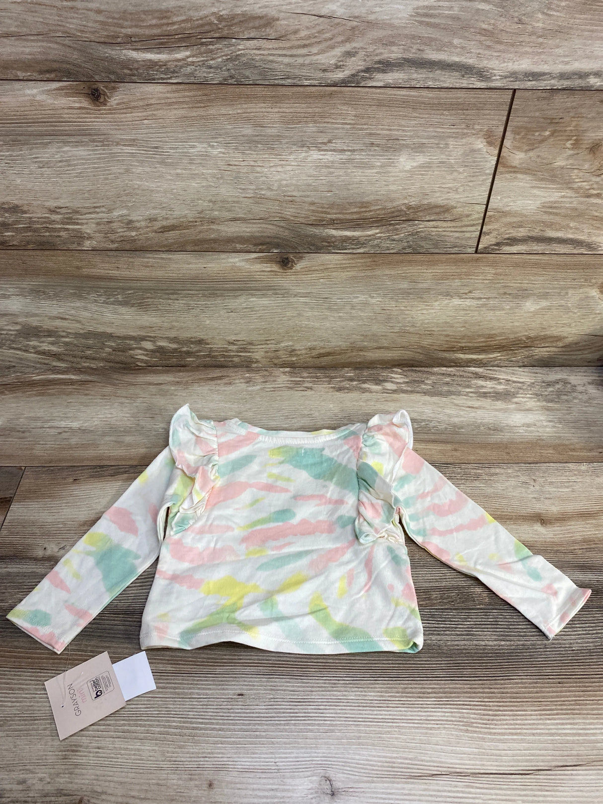 Pastel tie dye long sleeve baby shirt with ruffle shoulders on wood background